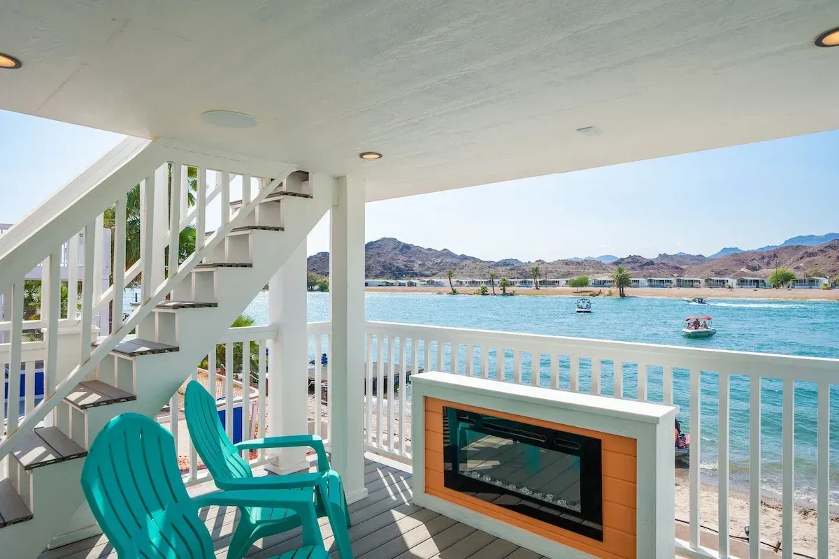 A balcony with two blue chairs and a fireplace overlooking a body of water.