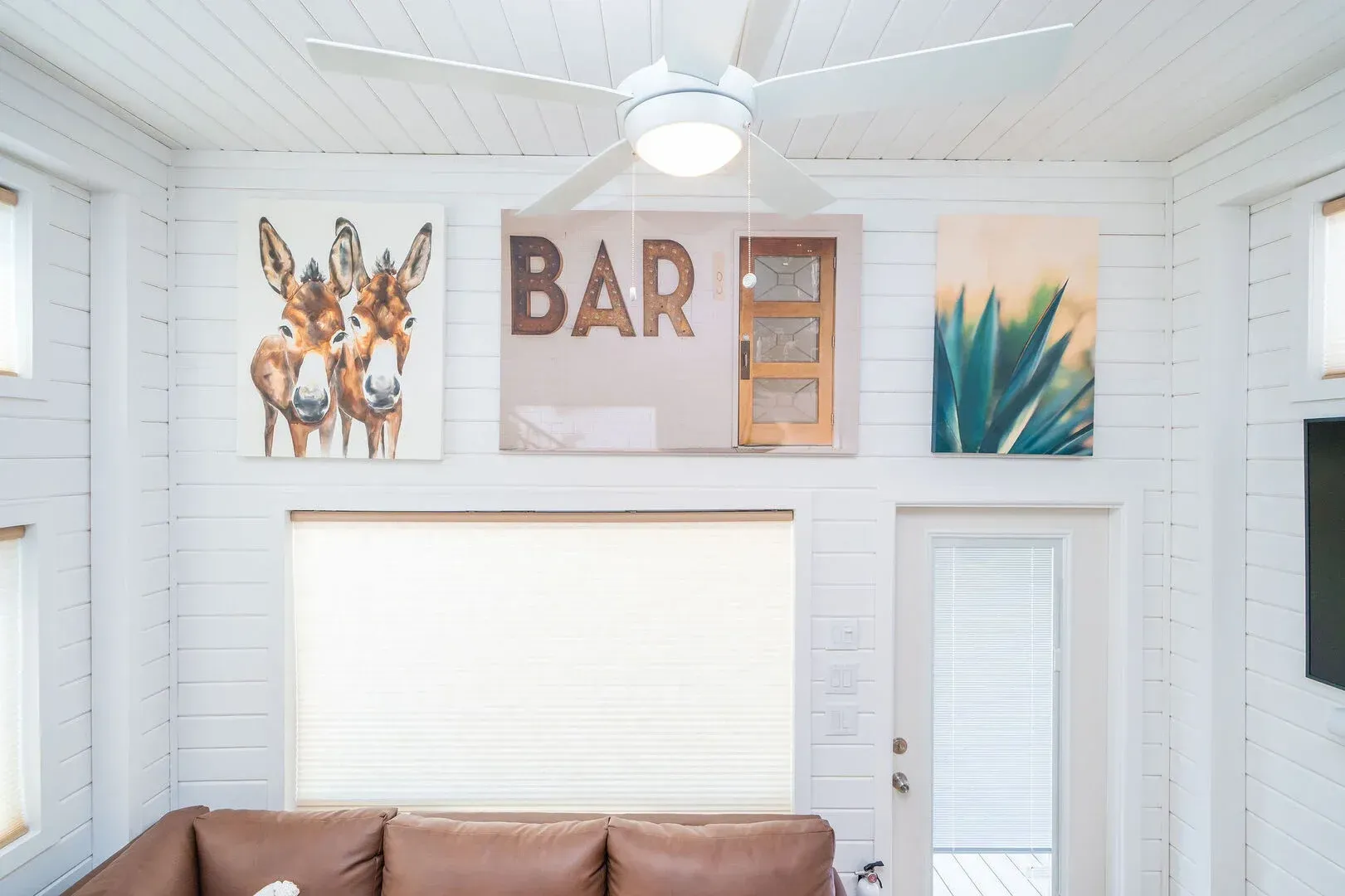 A living room with a ceiling fan and a bar sign on the wall.