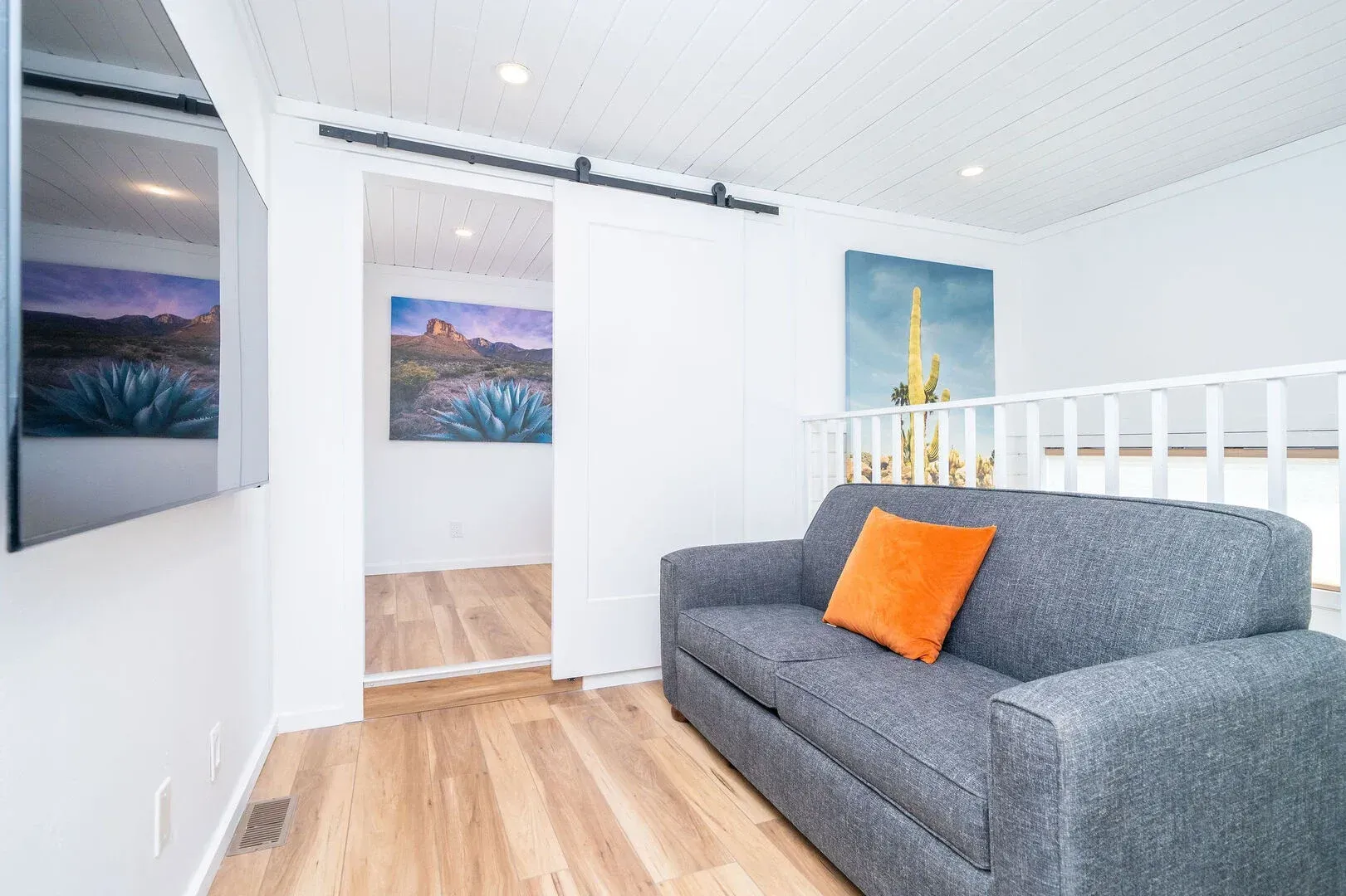 A living room with a couch , television and paintings on the wall.