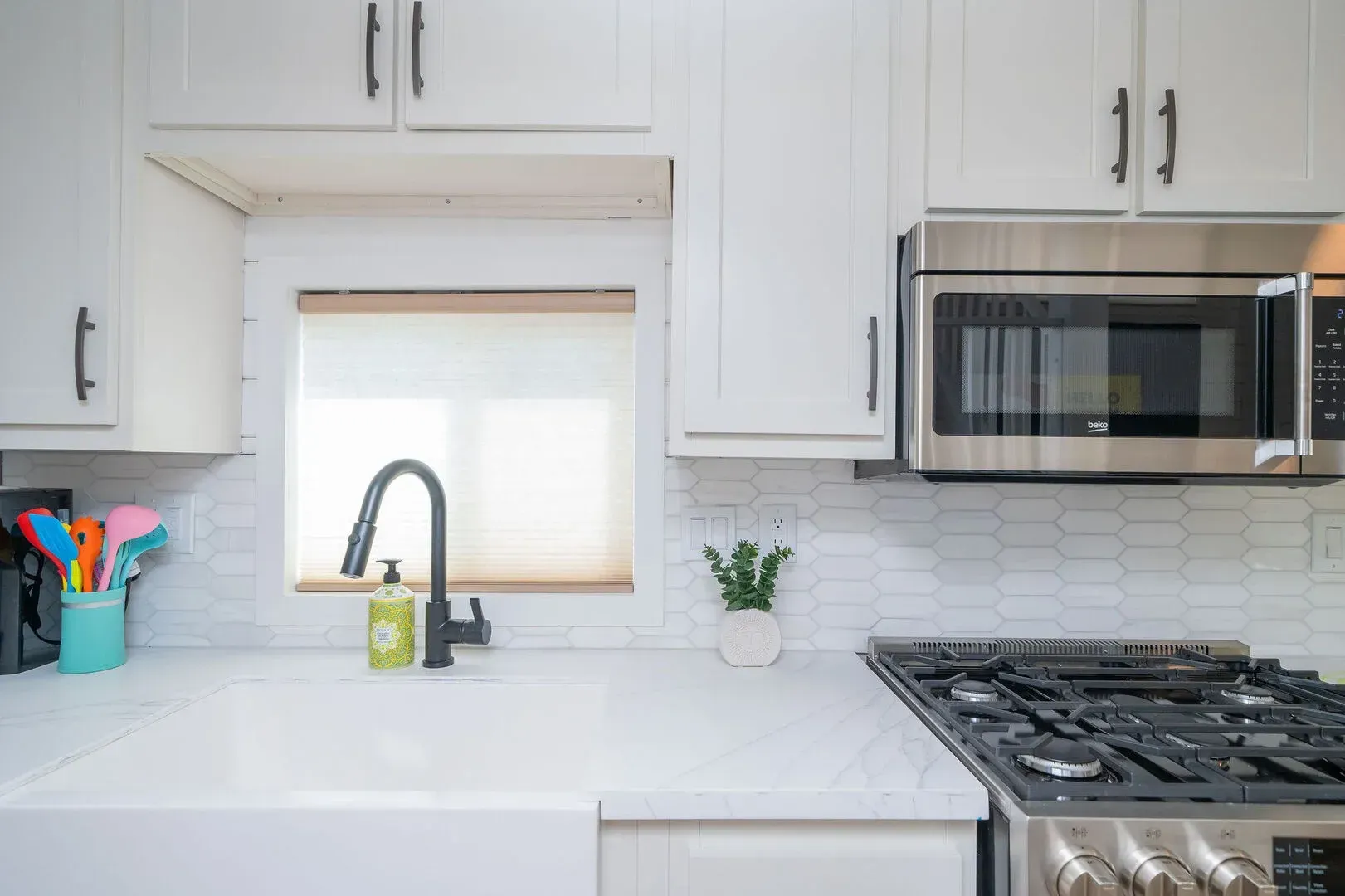 A kitchen with white cabinets , a stove , a sink , and a microwave.
