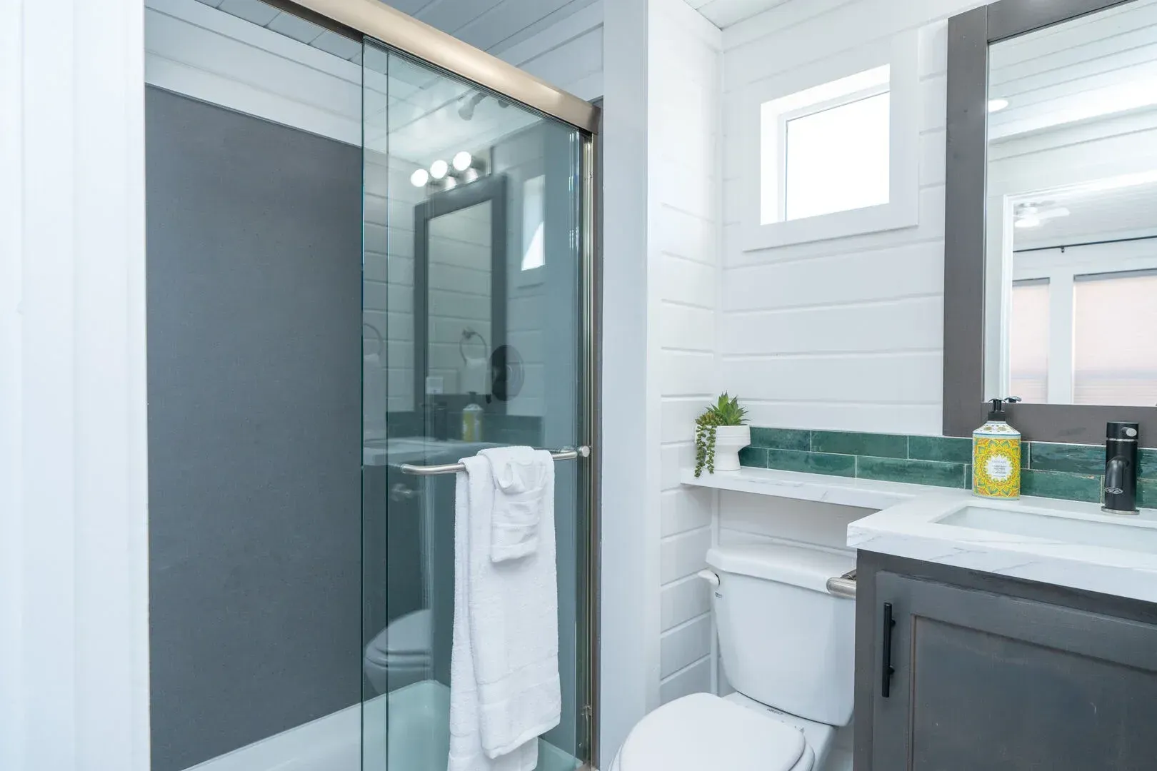 A bathroom with a toilet , sink , mirror and shower stall.