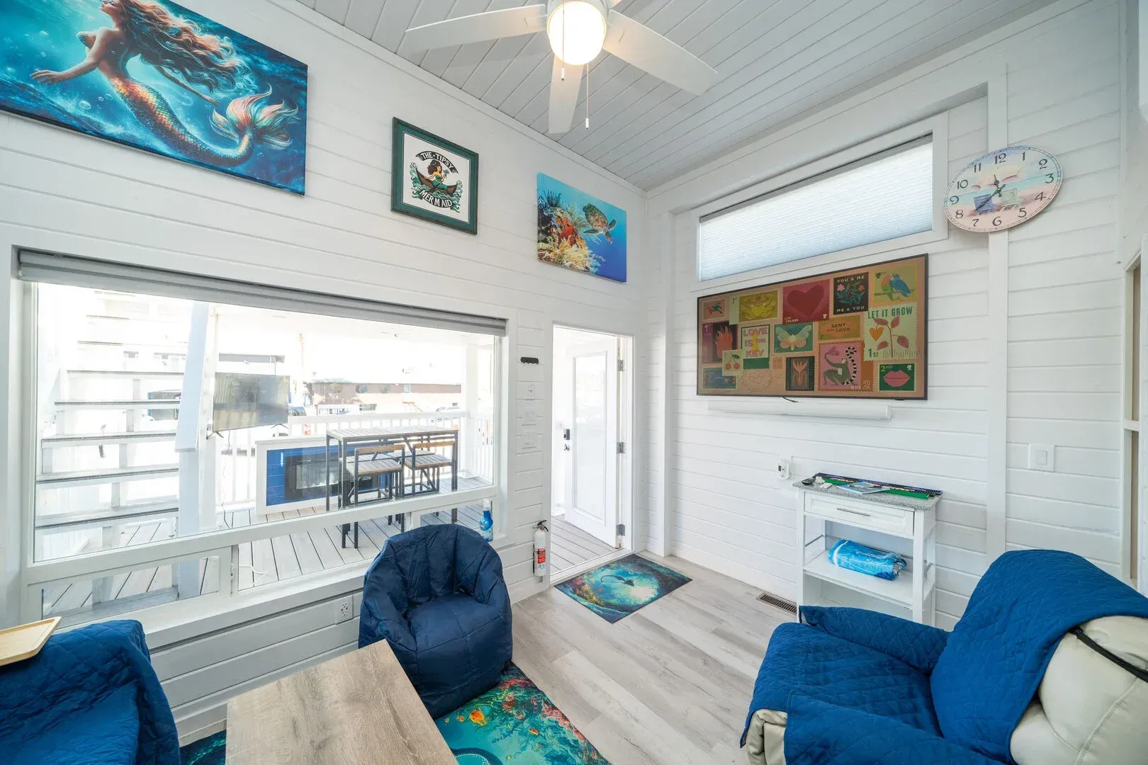 A living room with blue chairs , a table , and a ceiling fan.