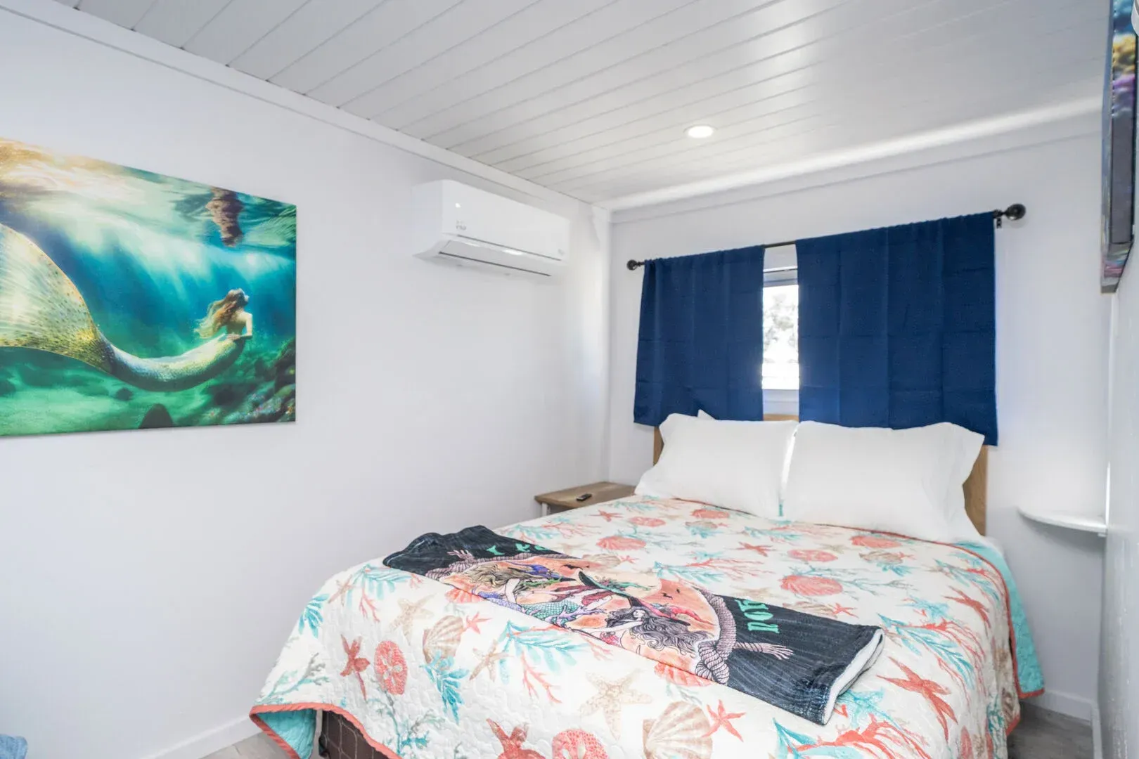 A bedroom with a bed and a painting of a mermaid on the wall.