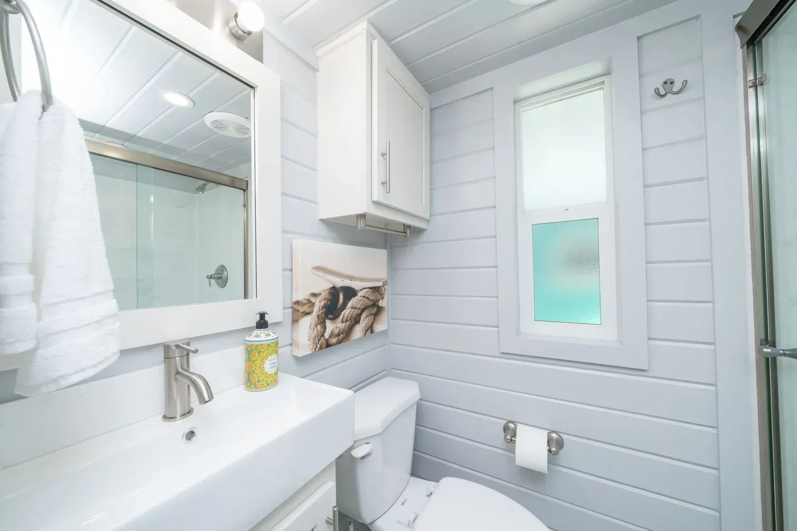 A bathroom with a toilet , sink , mirror and window.
