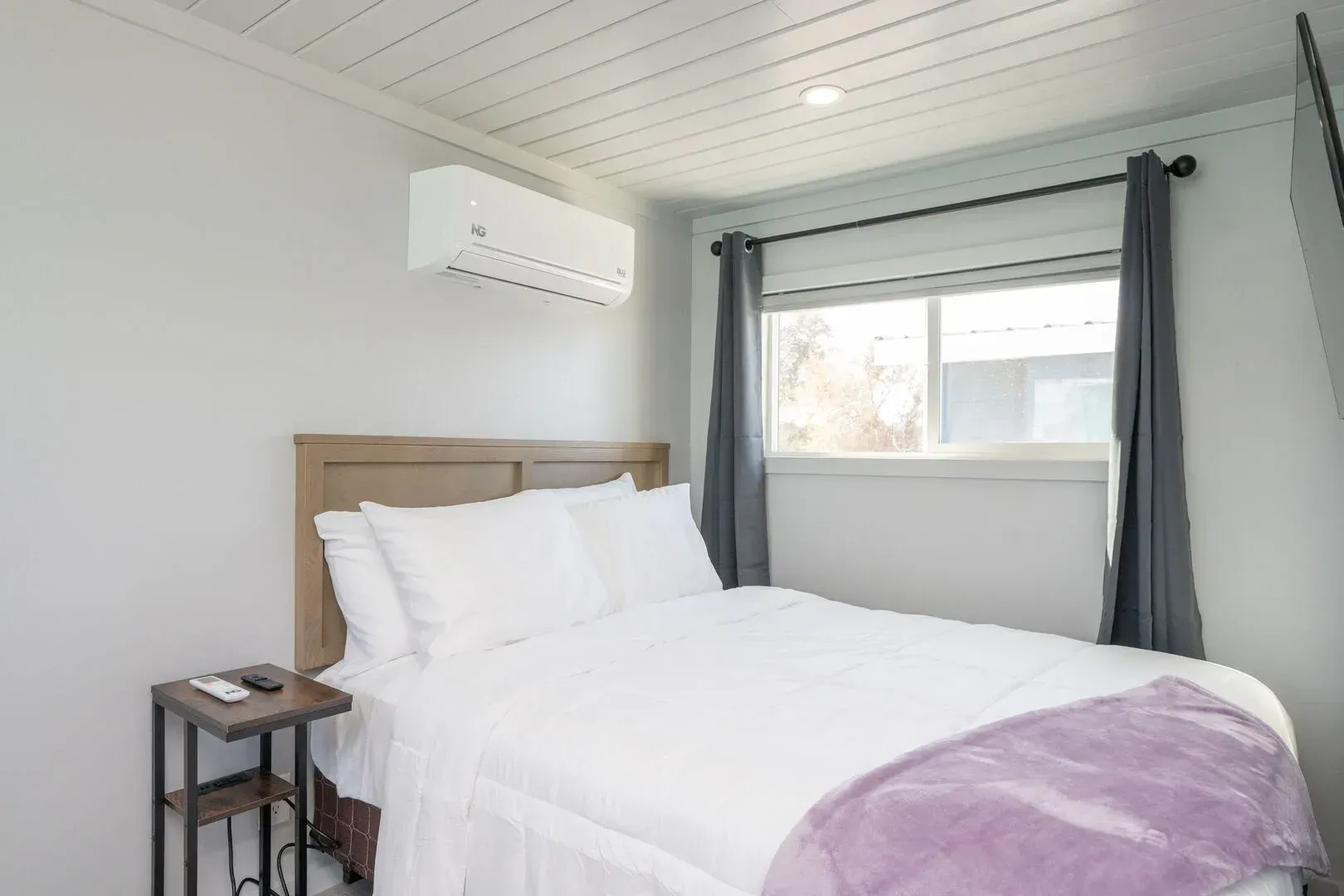 A bedroom with a bed , nightstand , window and air conditioner.