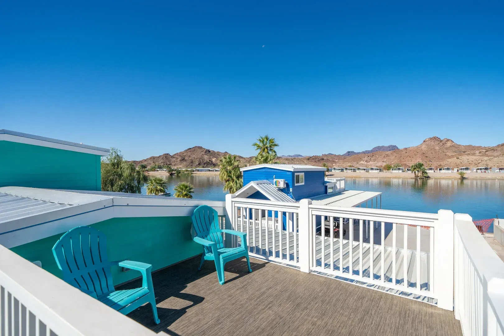 A balcony with blue chairs and a couch overlooking a lake.