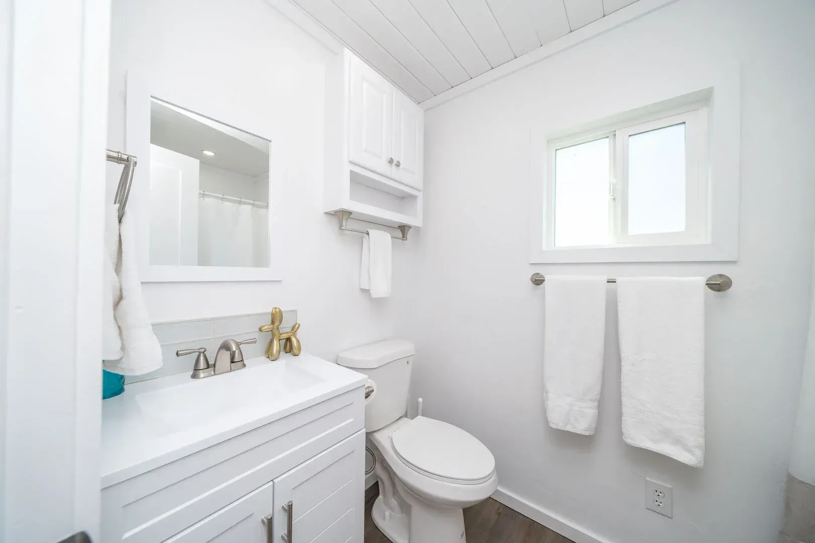 A bathroom with a toilet , sink , mirror and window.
