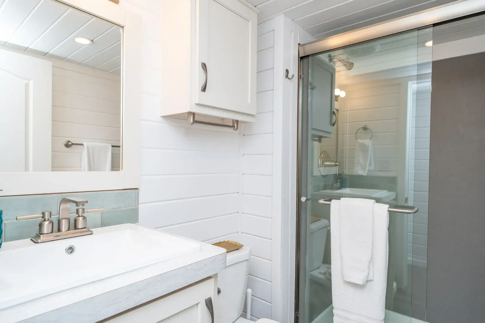 A bathroom with a sink , toilet , mirror and shower.