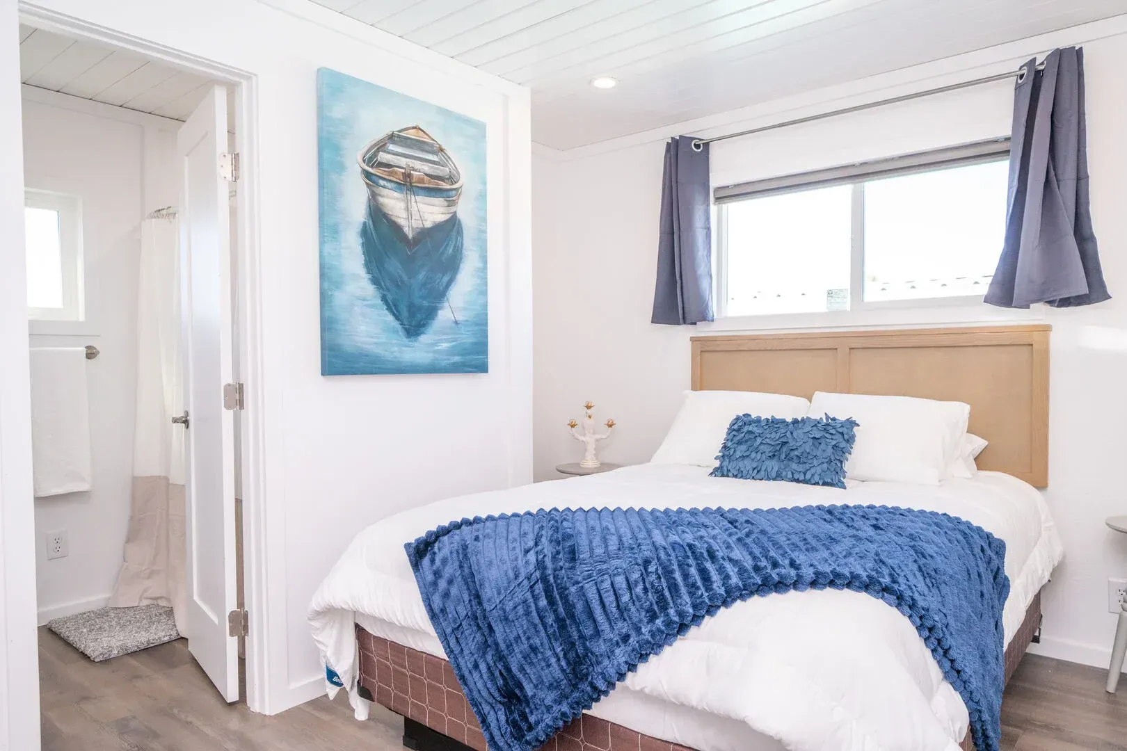 A bedroom with a bed and a painting of a boat on the wall.