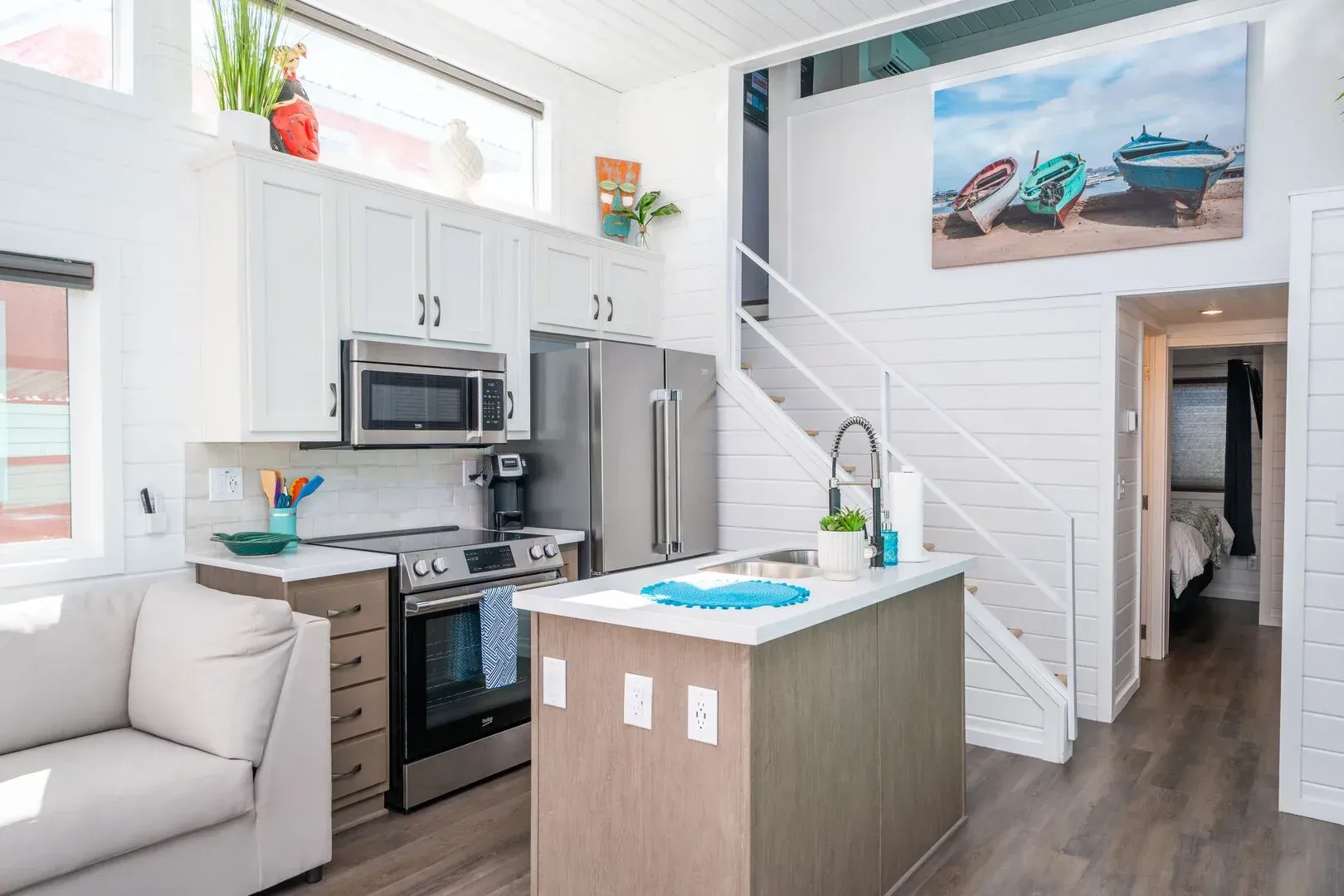A kitchen with stainless steel appliances , a large island , a couch , and a staircase.