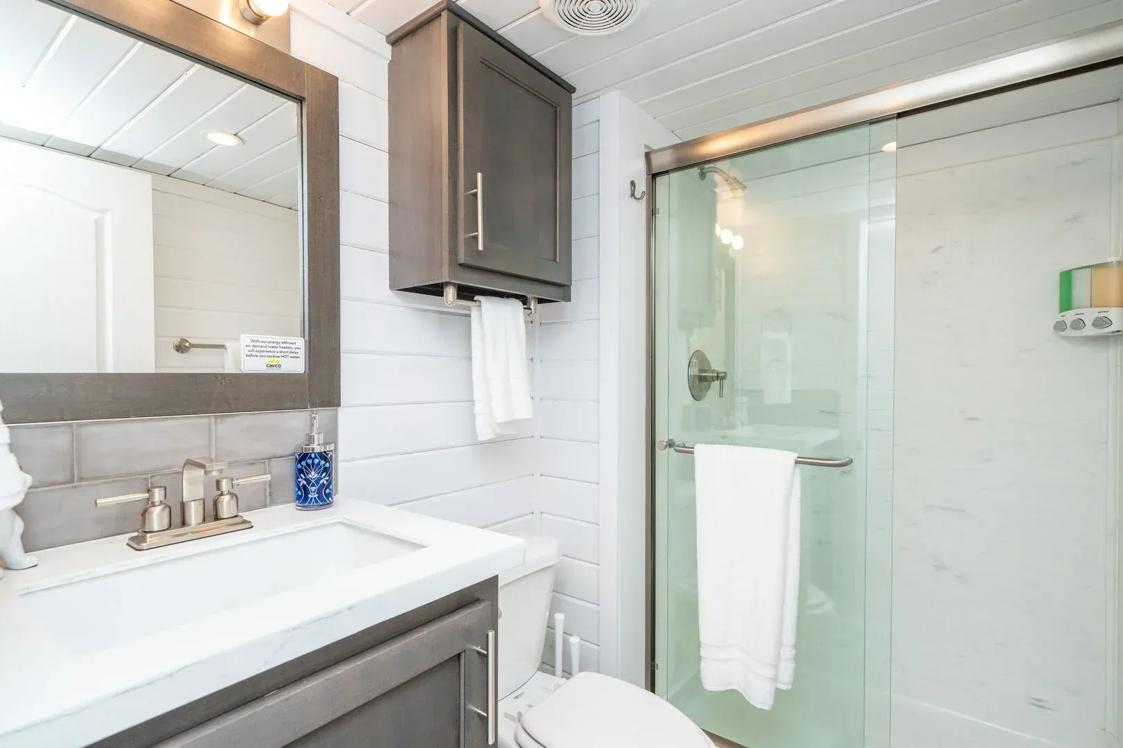 A bathroom with a toilet , sink , mirror and shower stall.