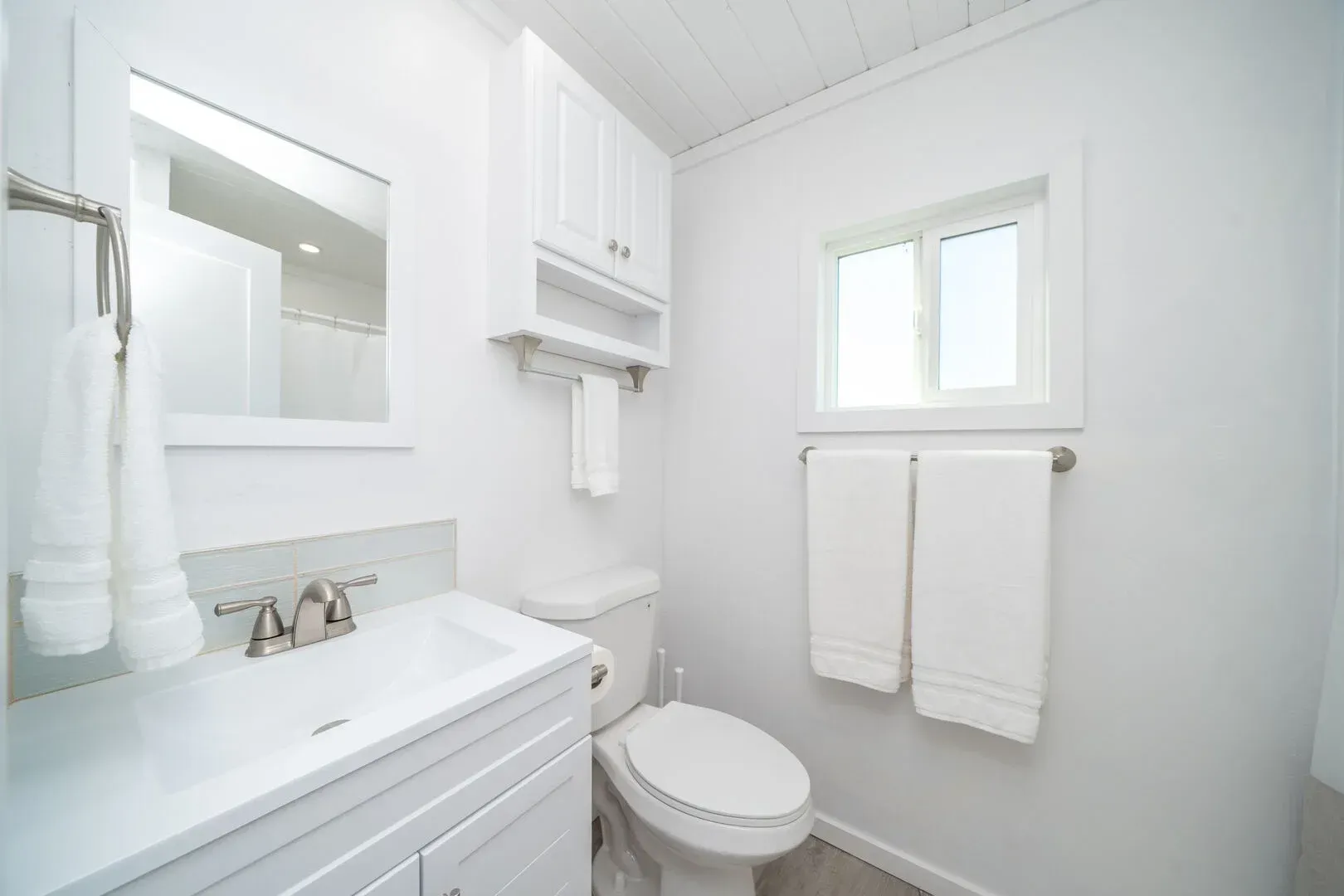 A bathroom with a toilet , sink , mirror and window.