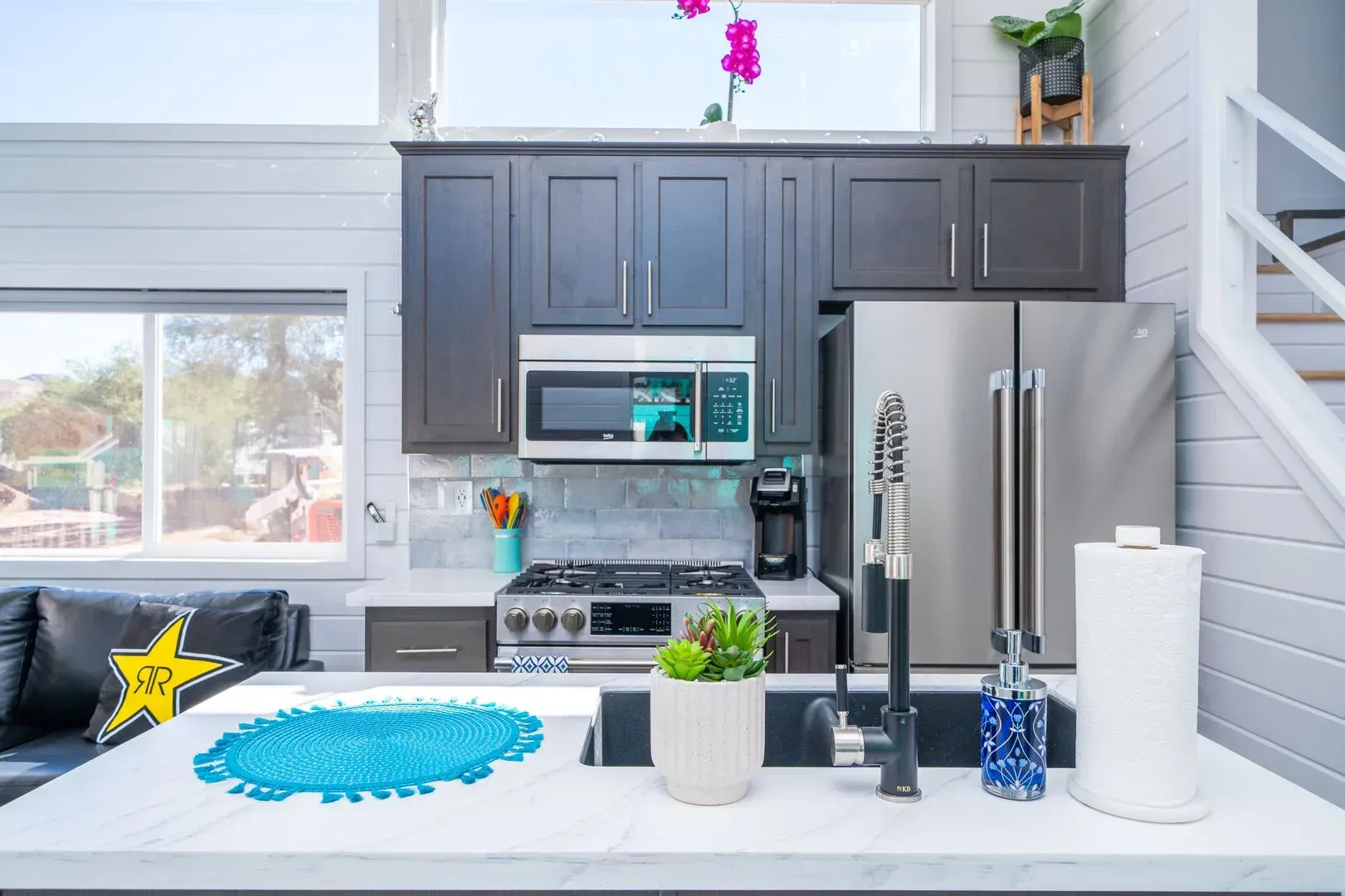 A kitchen with stainless steel appliances , black cabinets , a sink , stove , microwave and refrigerator.