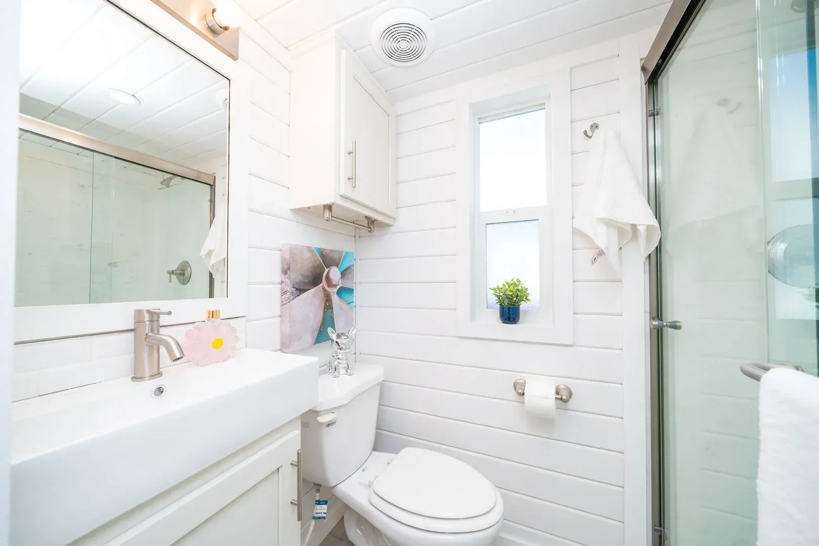 A bathroom with a toilet , sink , mirror and shower.
