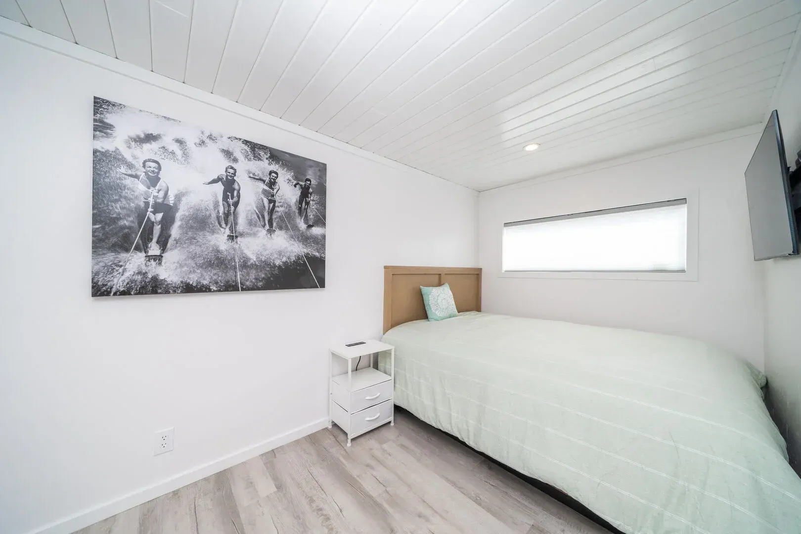 A bedroom with a bed , nightstand , television and a painting on the wall.