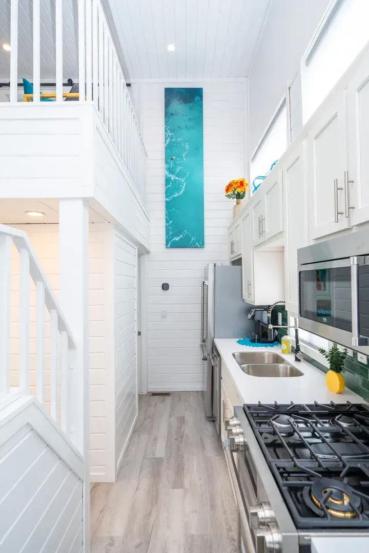 A kitchen with a stove , sink , microwave and stairs.