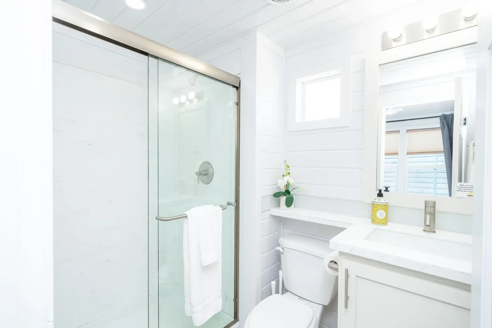 A bathroom with a toilet , sink , mirror and shower stall.
