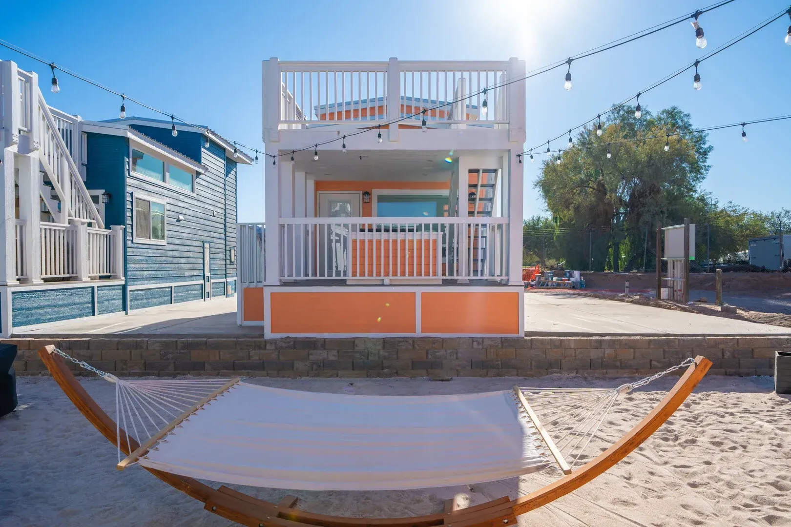 A hammock is sitting in front of a small house on the beach.