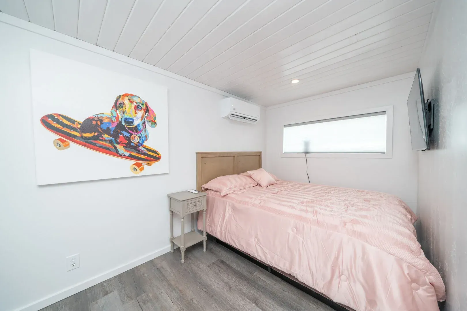 A bedroom with a bed and a painting of a dog on a skateboard.