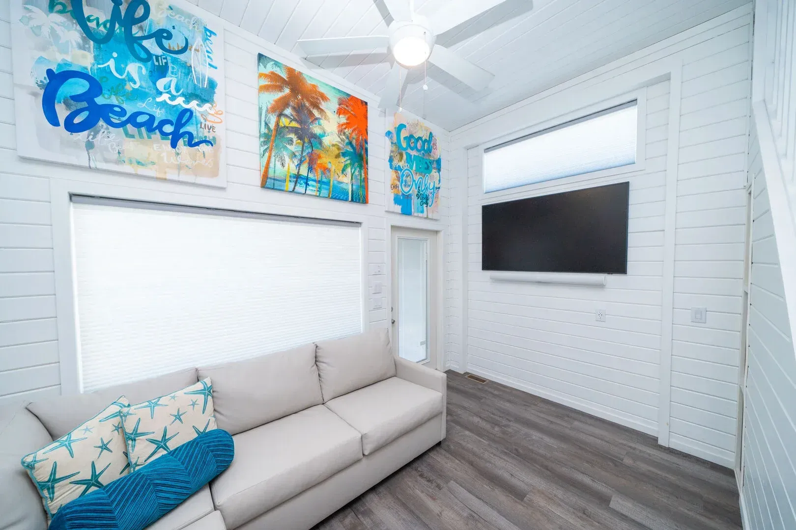 A living room with a couch , television and paintings on the wall.