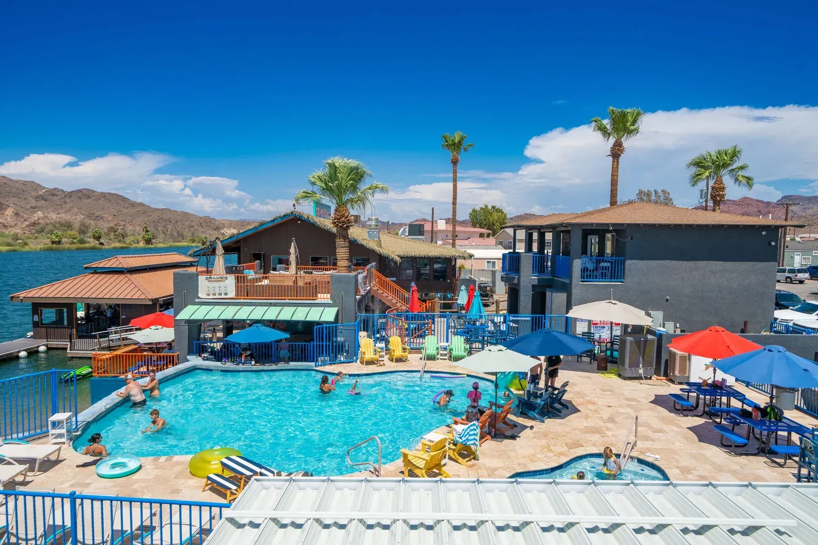 A large swimming pool surrounded by umbrellas and chairs with people swimming in it.