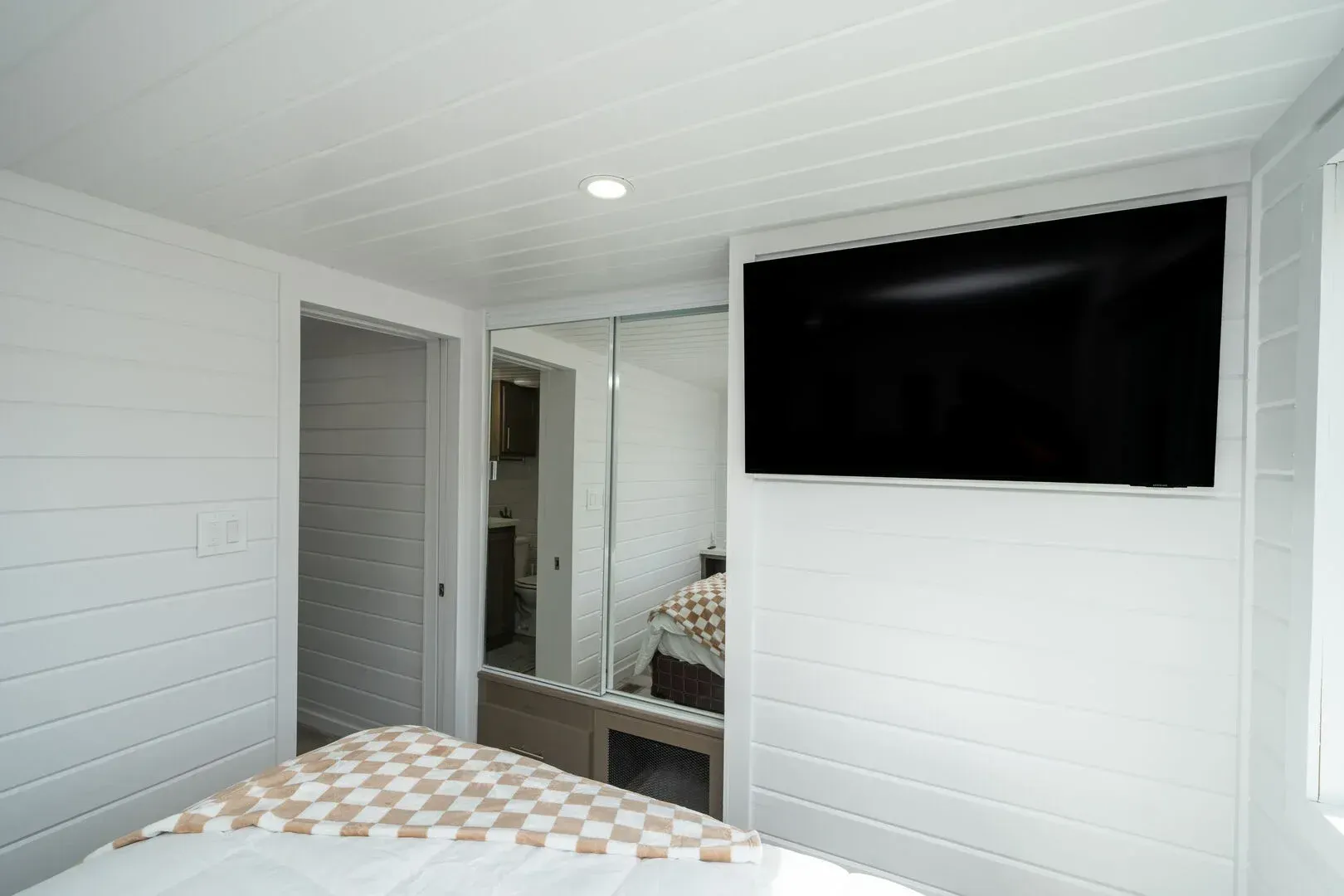 A bedroom with a bed and a flat screen tv on the wall.