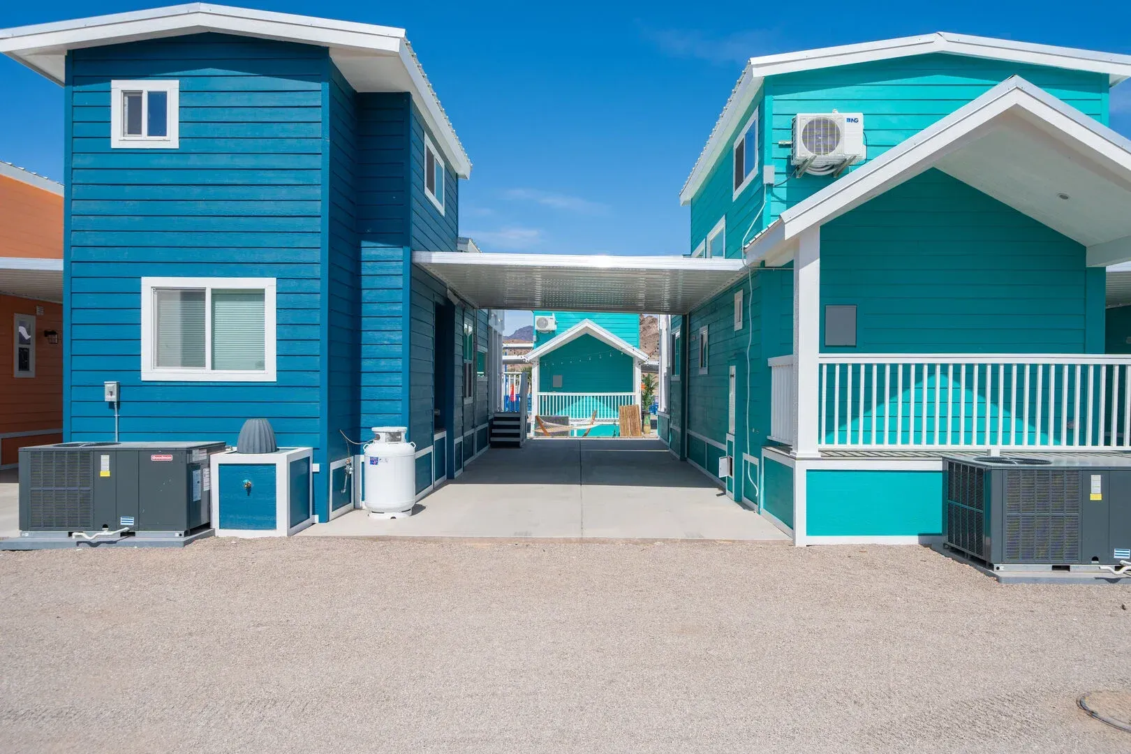 Two blue houses are next to each other on a dirt road
