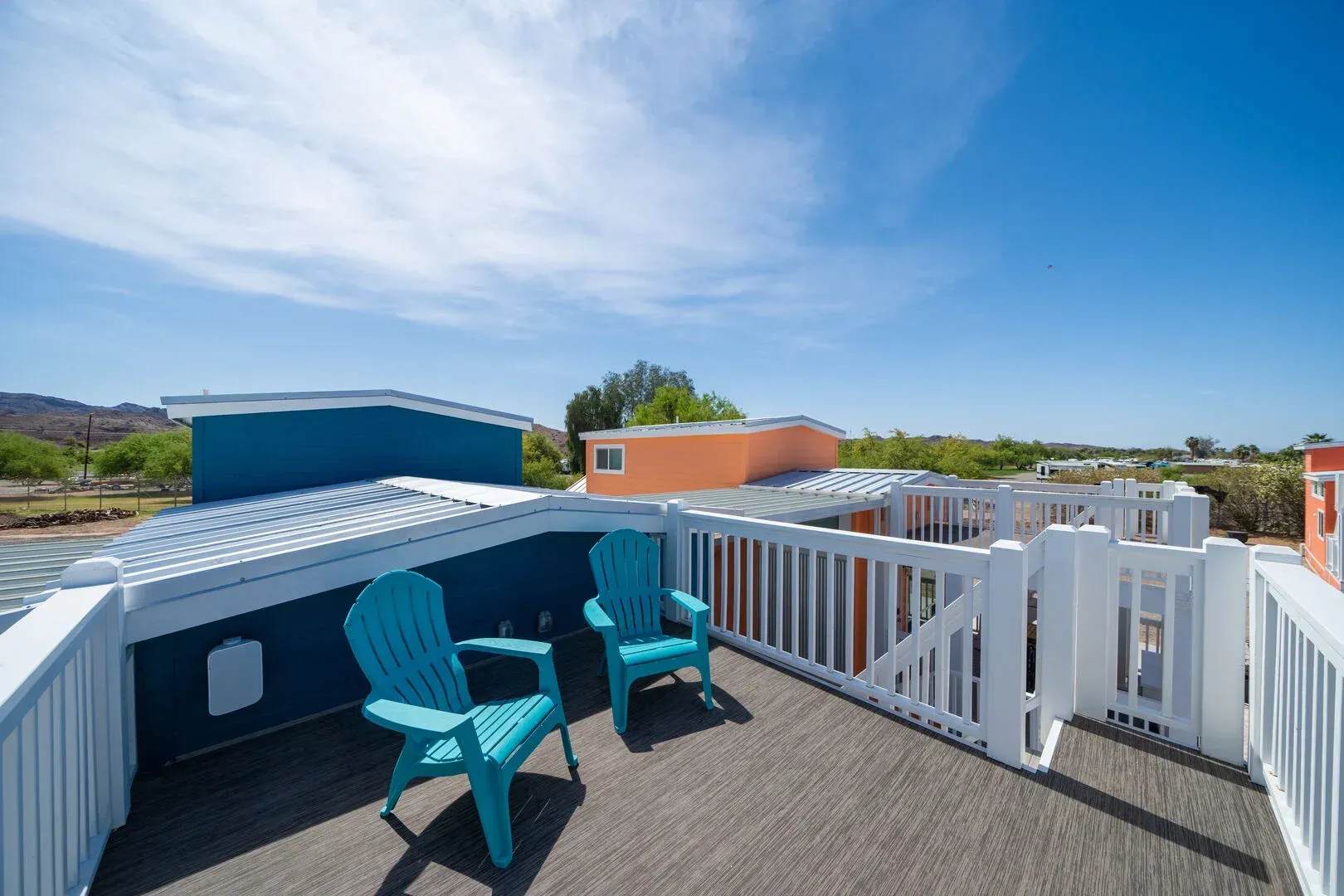 A balcony with two blue chairs and a white railing.