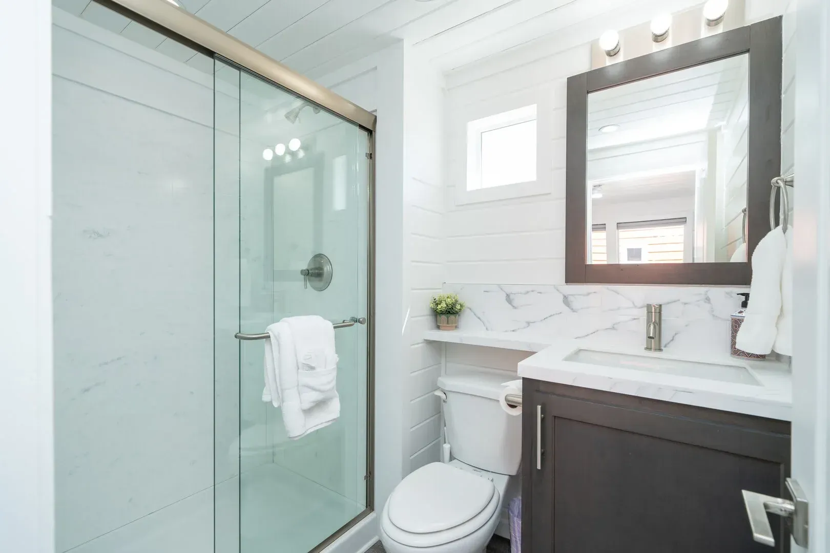 A bathroom with a toilet , sink , mirror and shower.