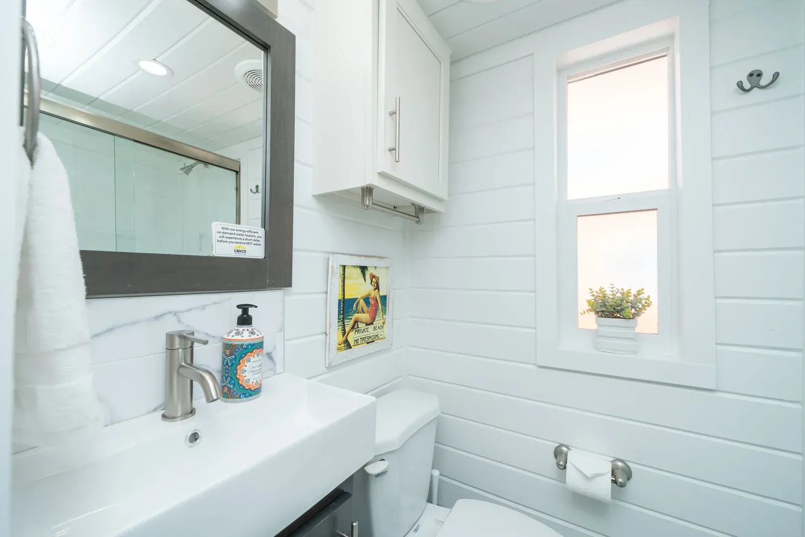 A bathroom with a toilet , sink , mirror and window.