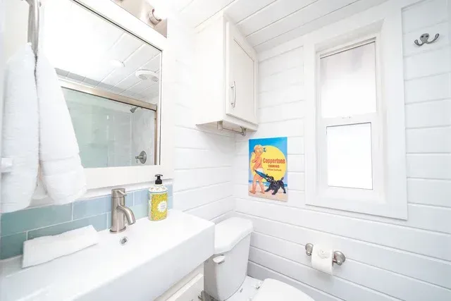A bathroom with a toilet , sink , mirror and window.