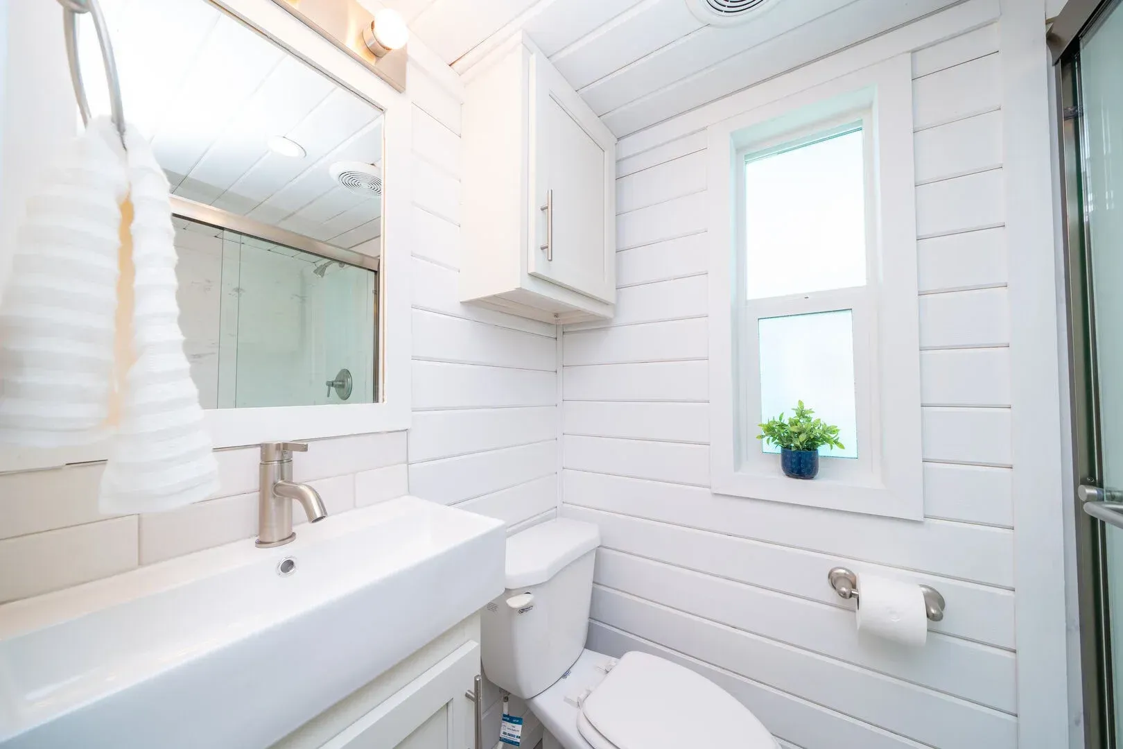 A bathroom with a toilet , sink , mirror and window.