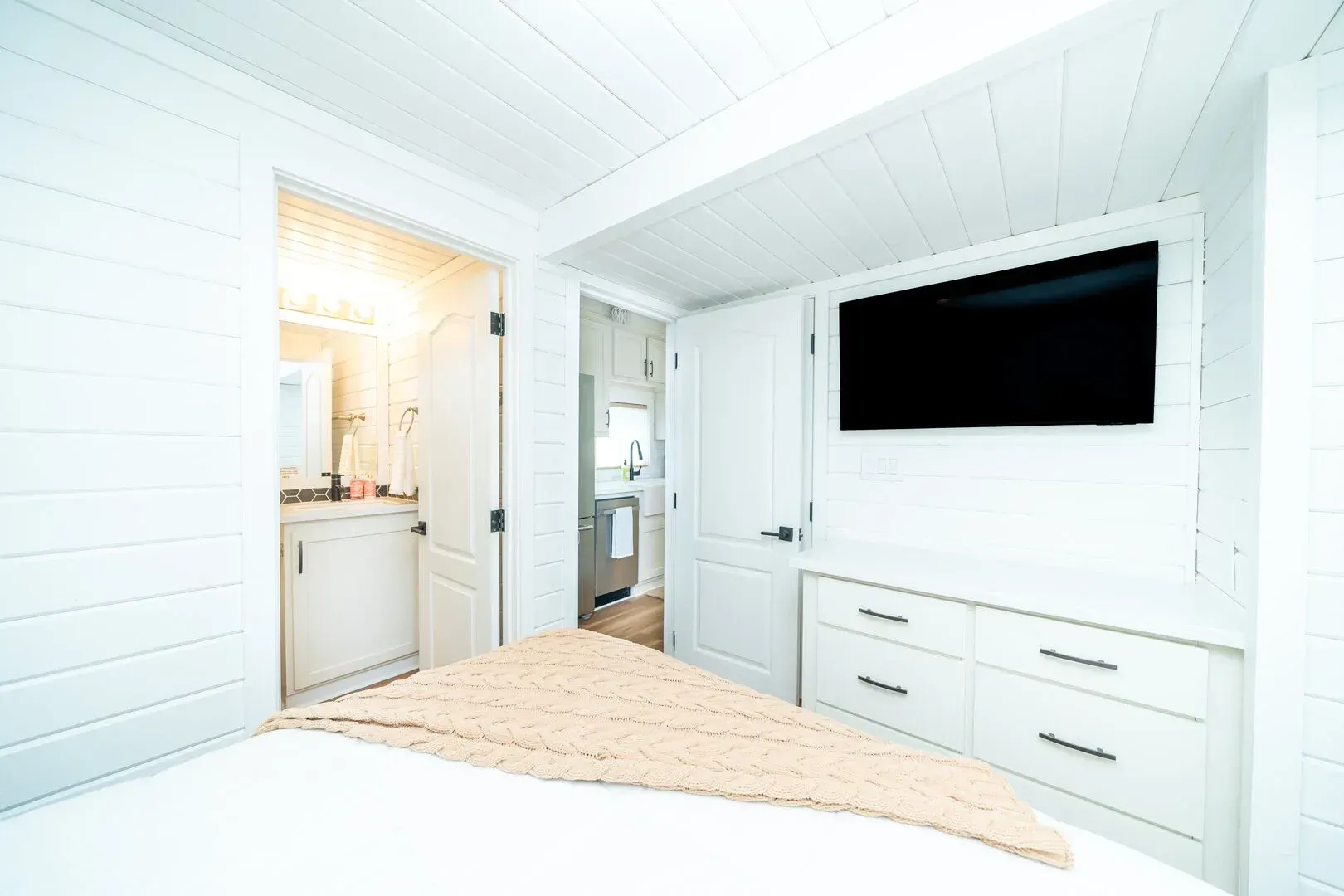 A bedroom with a bed , dresser , television and bathroom.