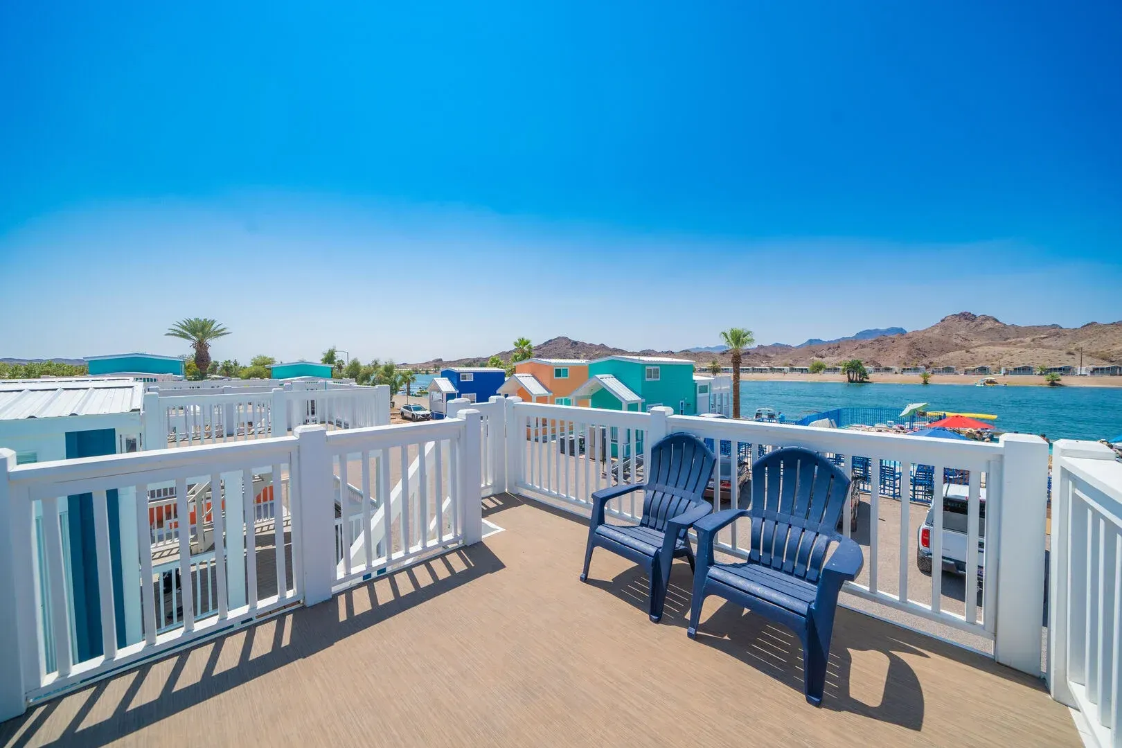 A balcony with two blue chairs and a white railing overlooking a body of water.