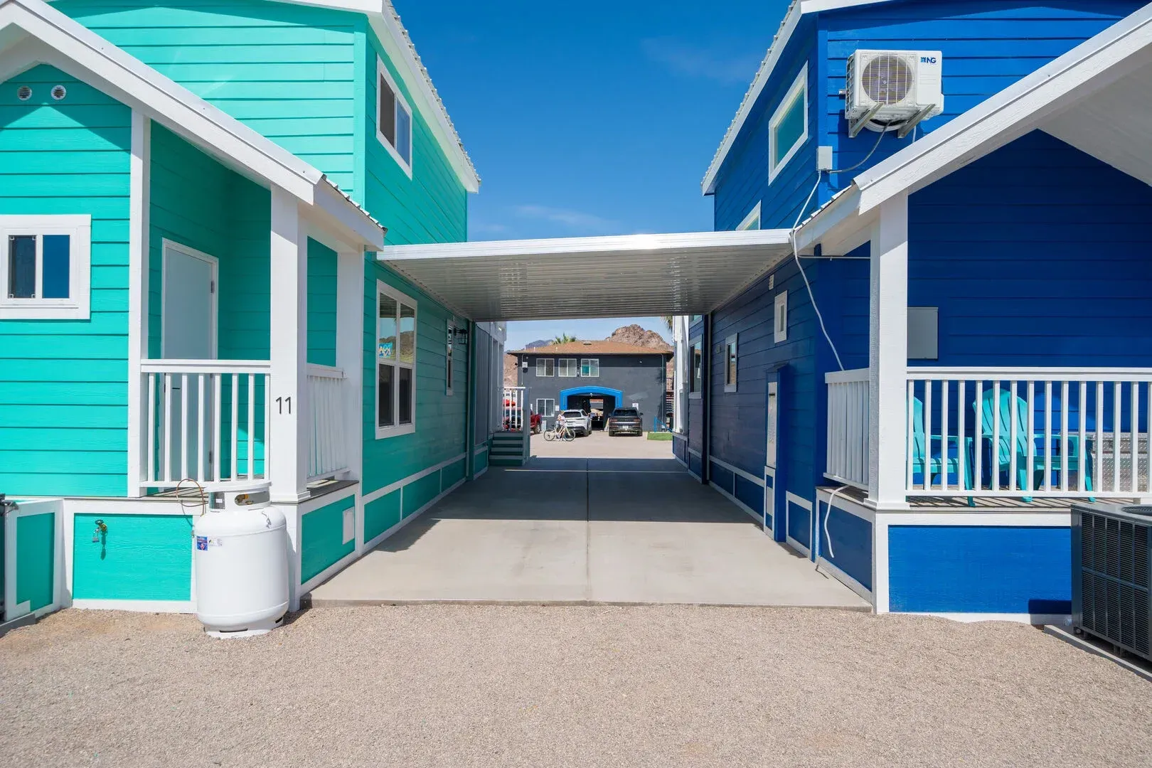 A blue and teal house with a carport between them.