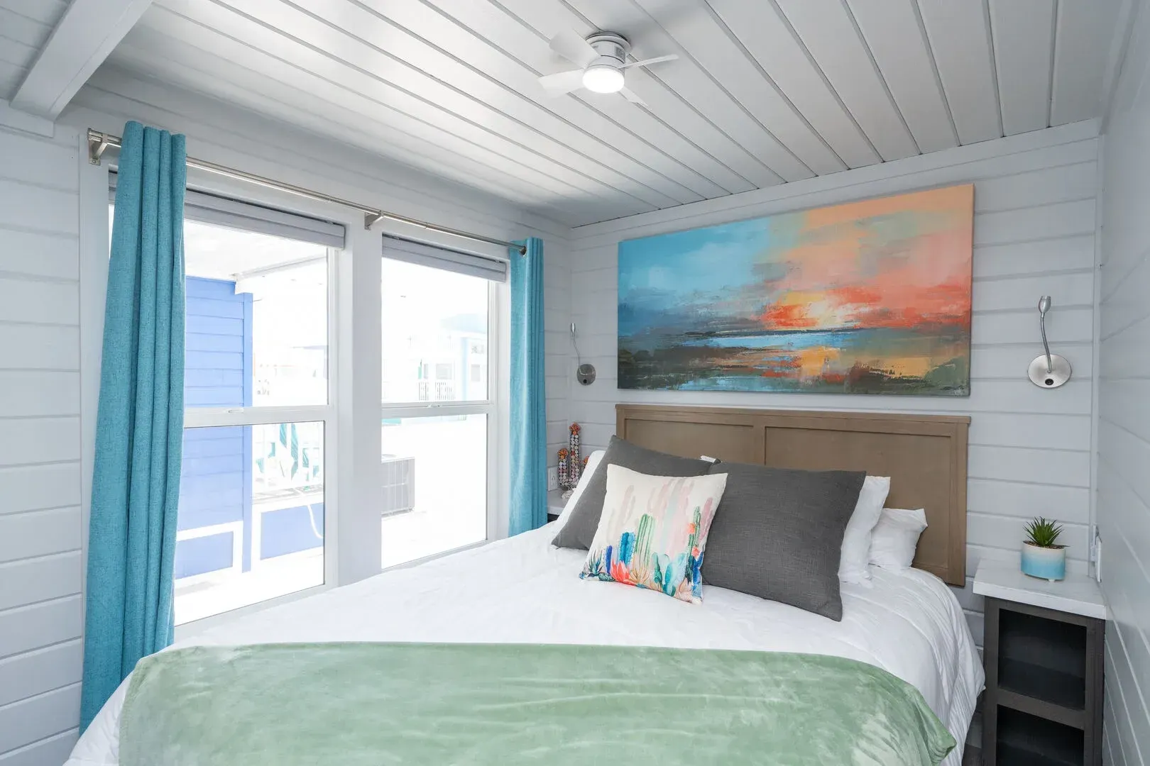 A bedroom with a large bed , a painting on the wall , and a ceiling fan.