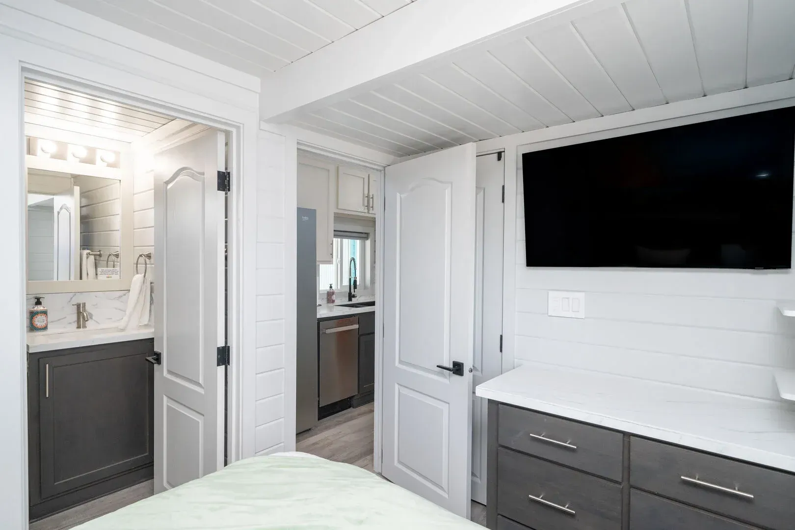 A bedroom with a bed , dresser , television and bathroom.