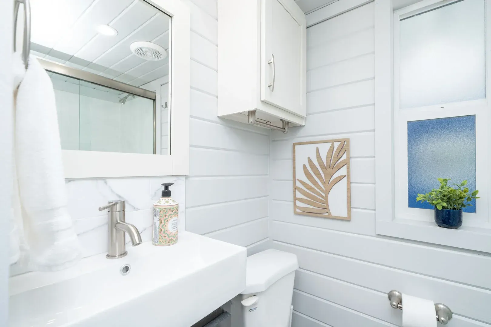 A bathroom with a sink , toilet , mirror and window.