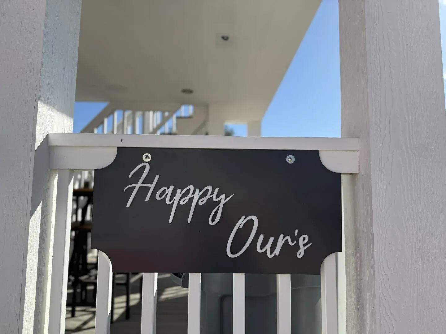 A black sign that says happy our 's on a white railing