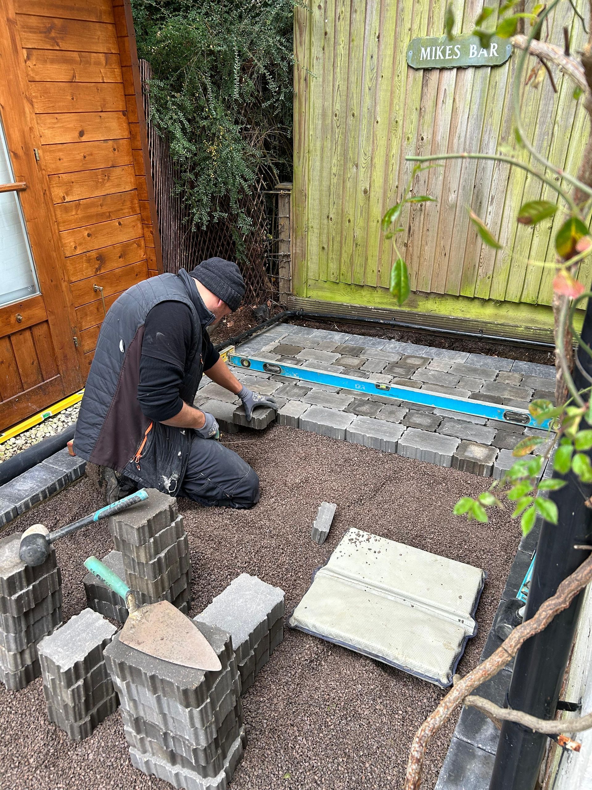 A man is kneeling down in a garden laying bricks.