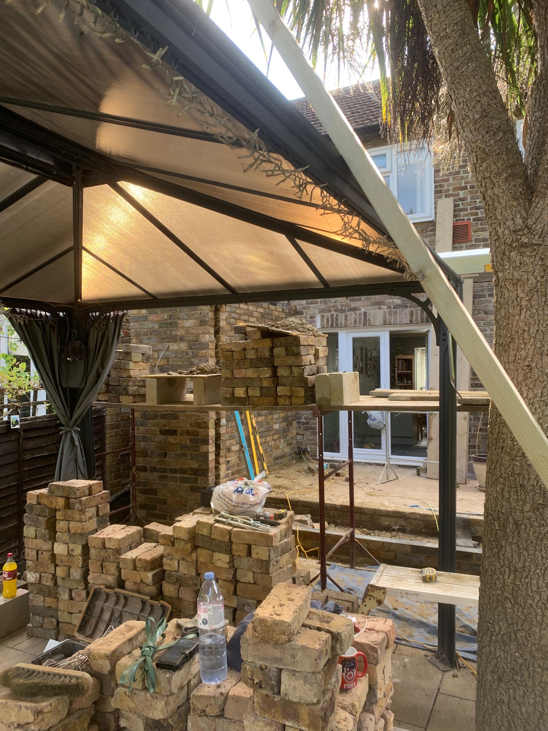 A pile of bricks is sitting under a canopy in a backyard.