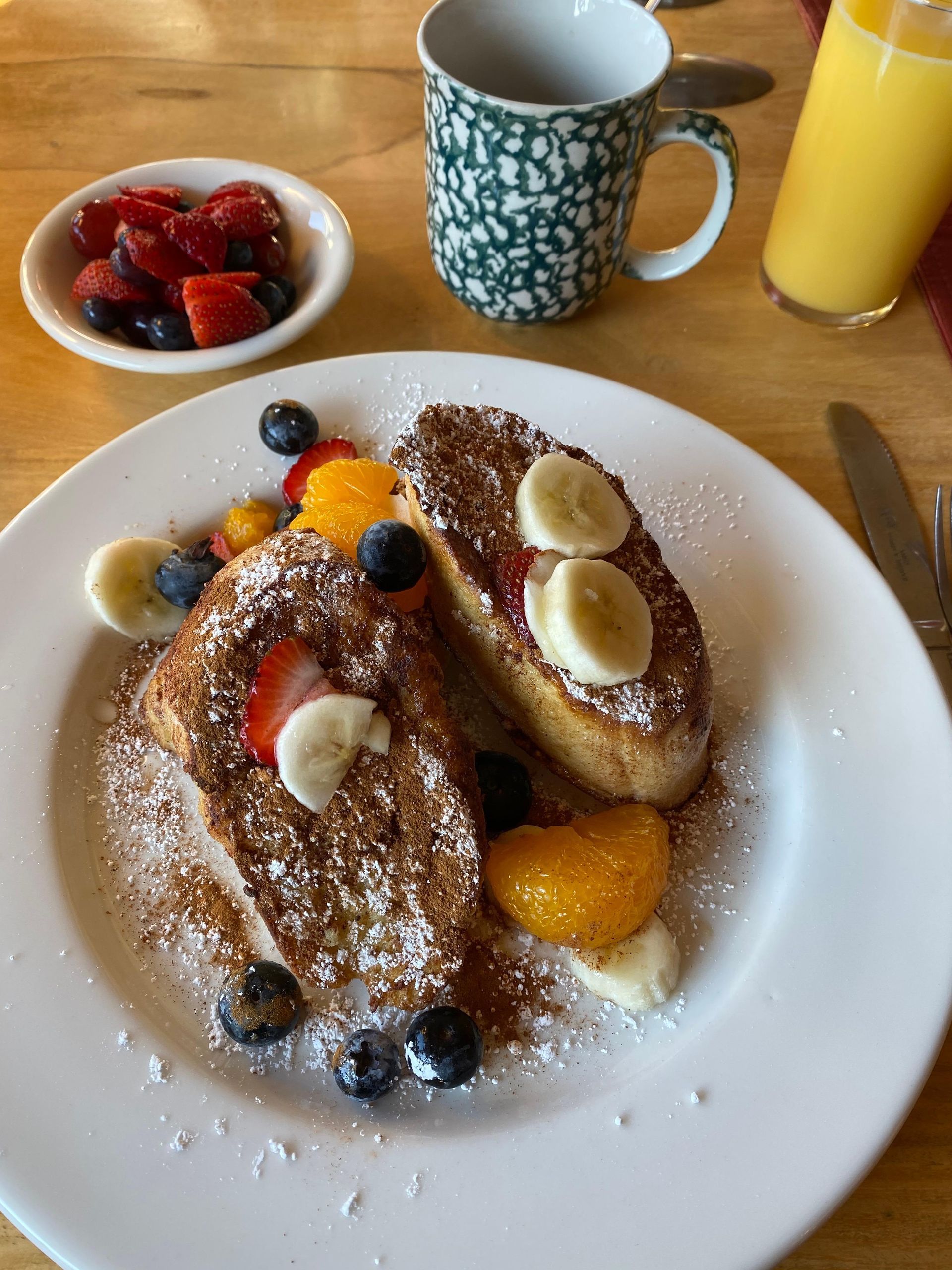 A plate of french toast with bananas strawberries and blueberries