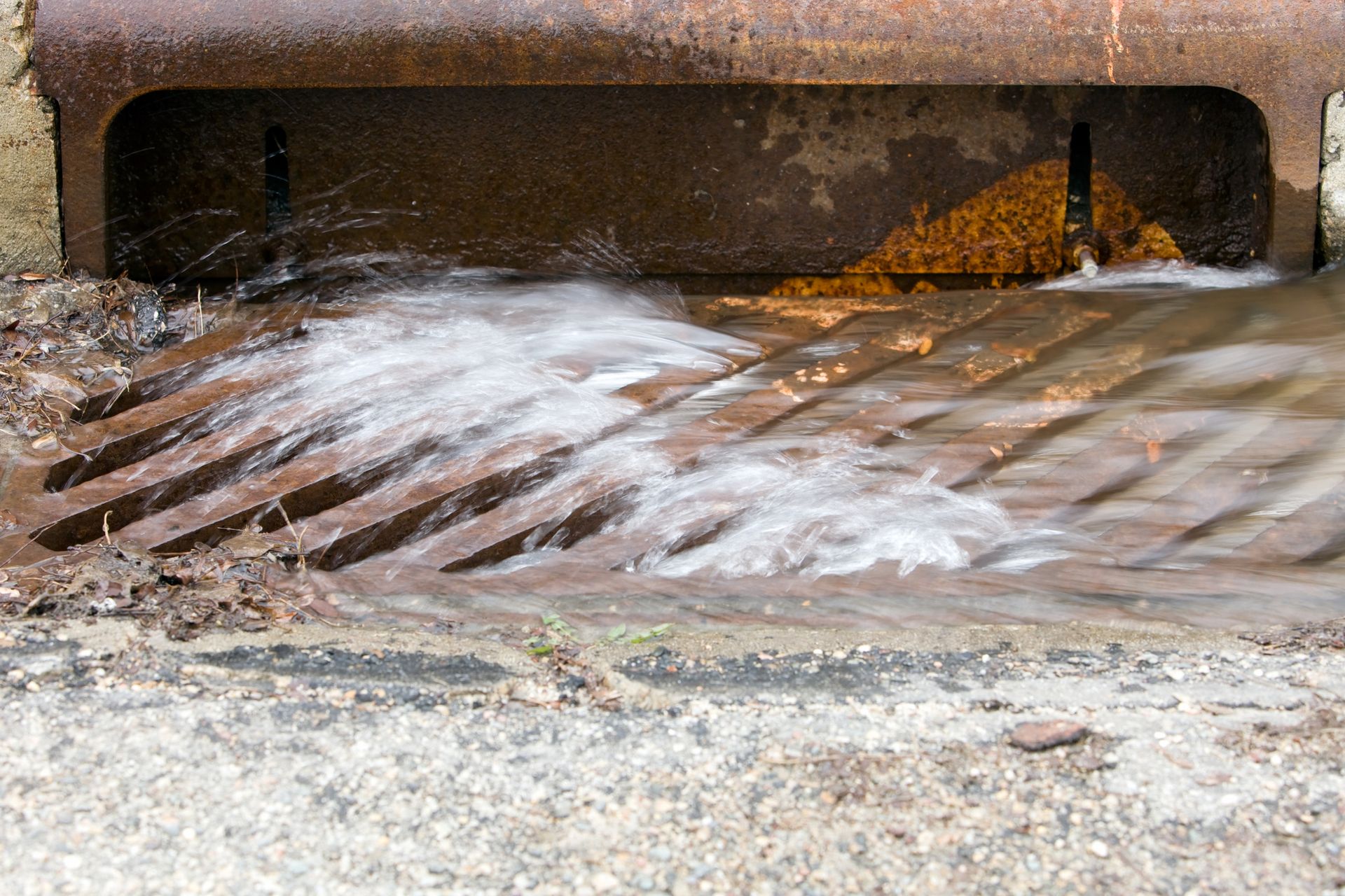 Water rushing into a rusty storm drain on a concrete curb.