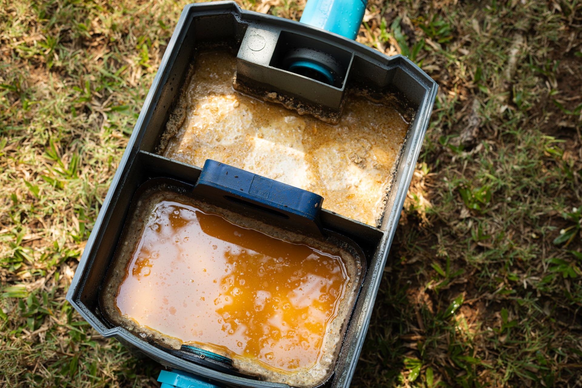 Open irrigation system component filled with brown liquid, set in grass.