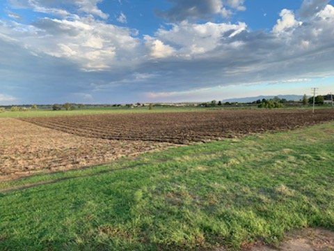 Plowed field, transitioning to green grass, under a partly cloudy sky.