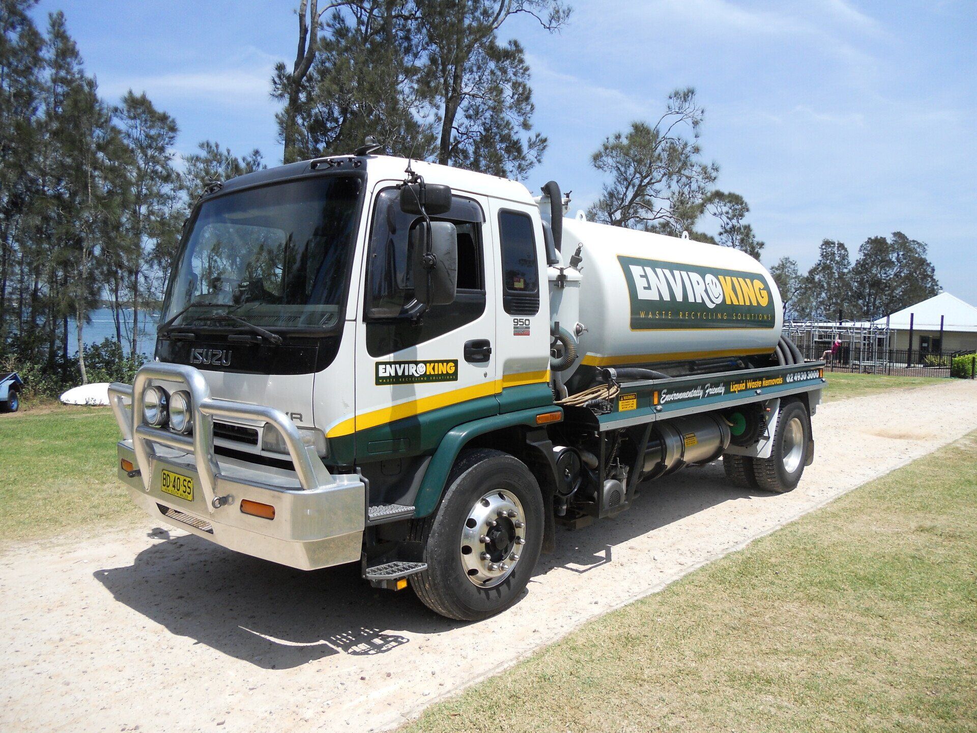 White and green Isuzu truck with a water tank parked on a gravel road, sunny day.