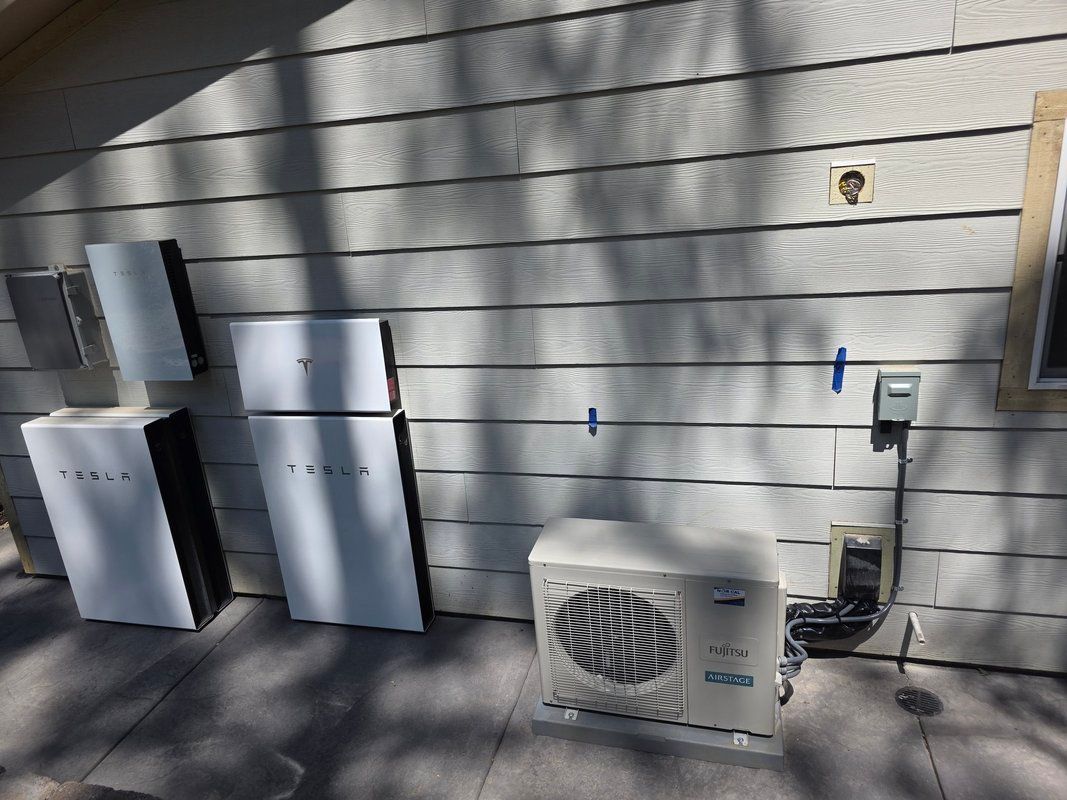 Solar panels and battery storage units installed on a house exterior next to an air conditioning unit.