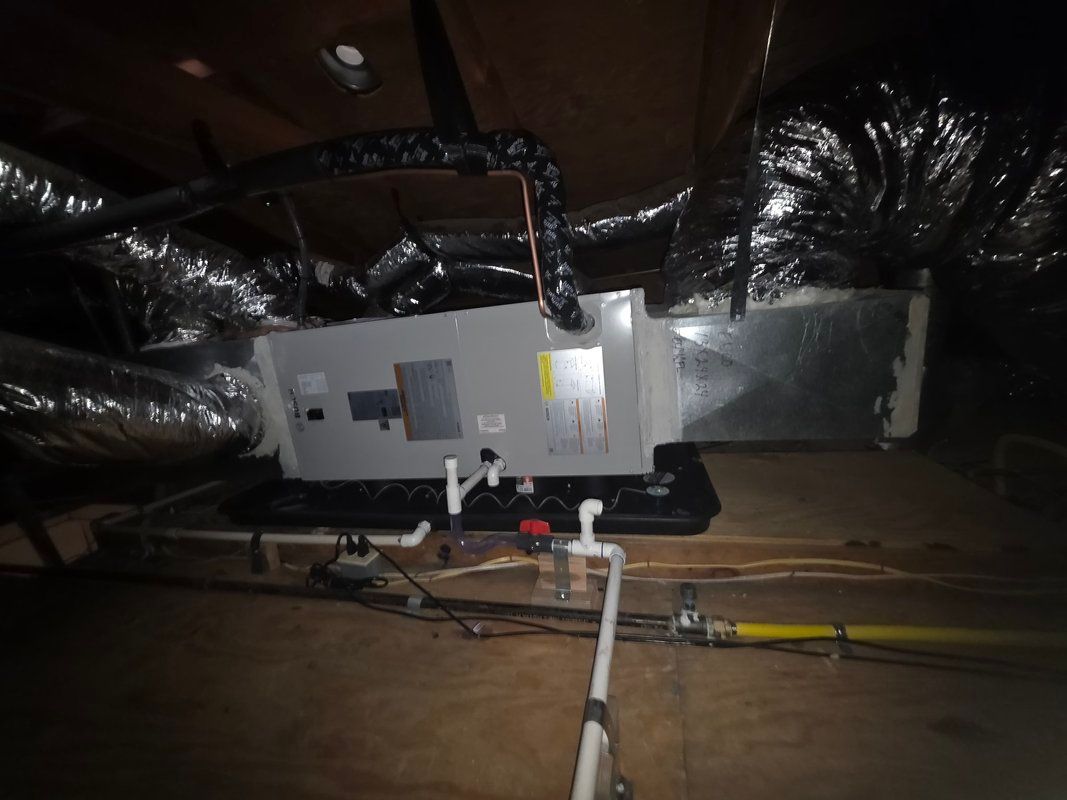 HVAC unit in an attic with ductwork and piping. Black insulation and silver ducting are visible.