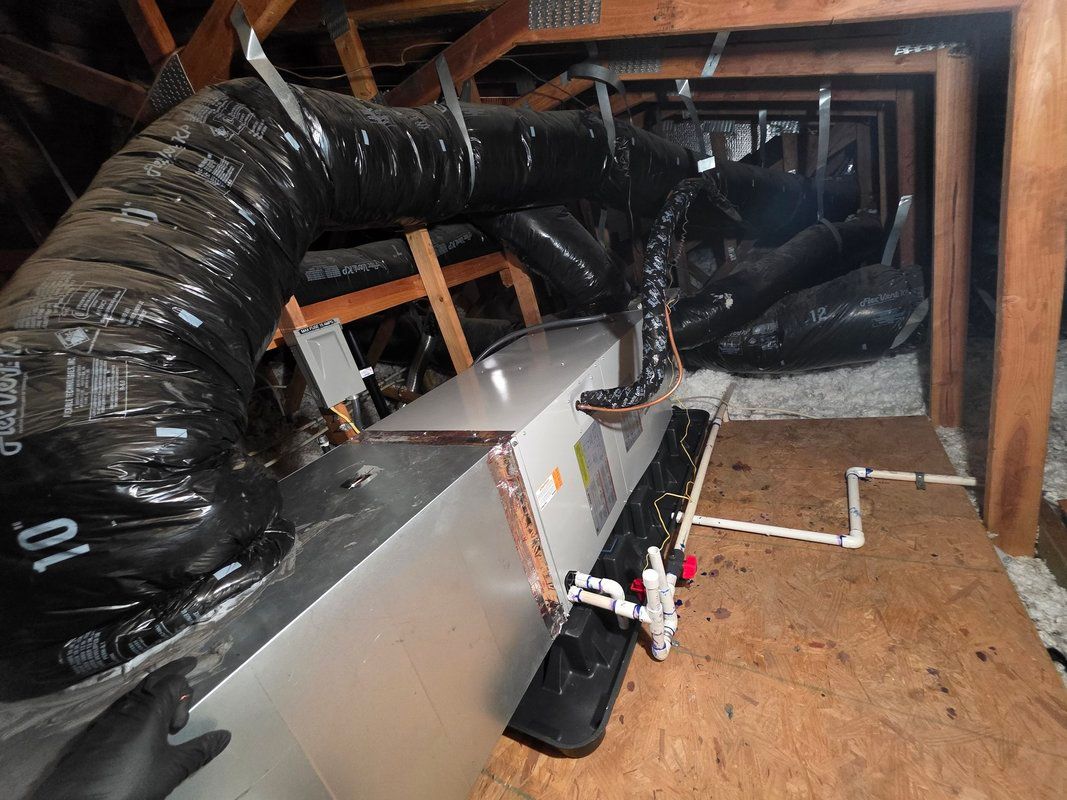 HVAC unit in an attic with black ductwork, wooden beams, and white pipes.