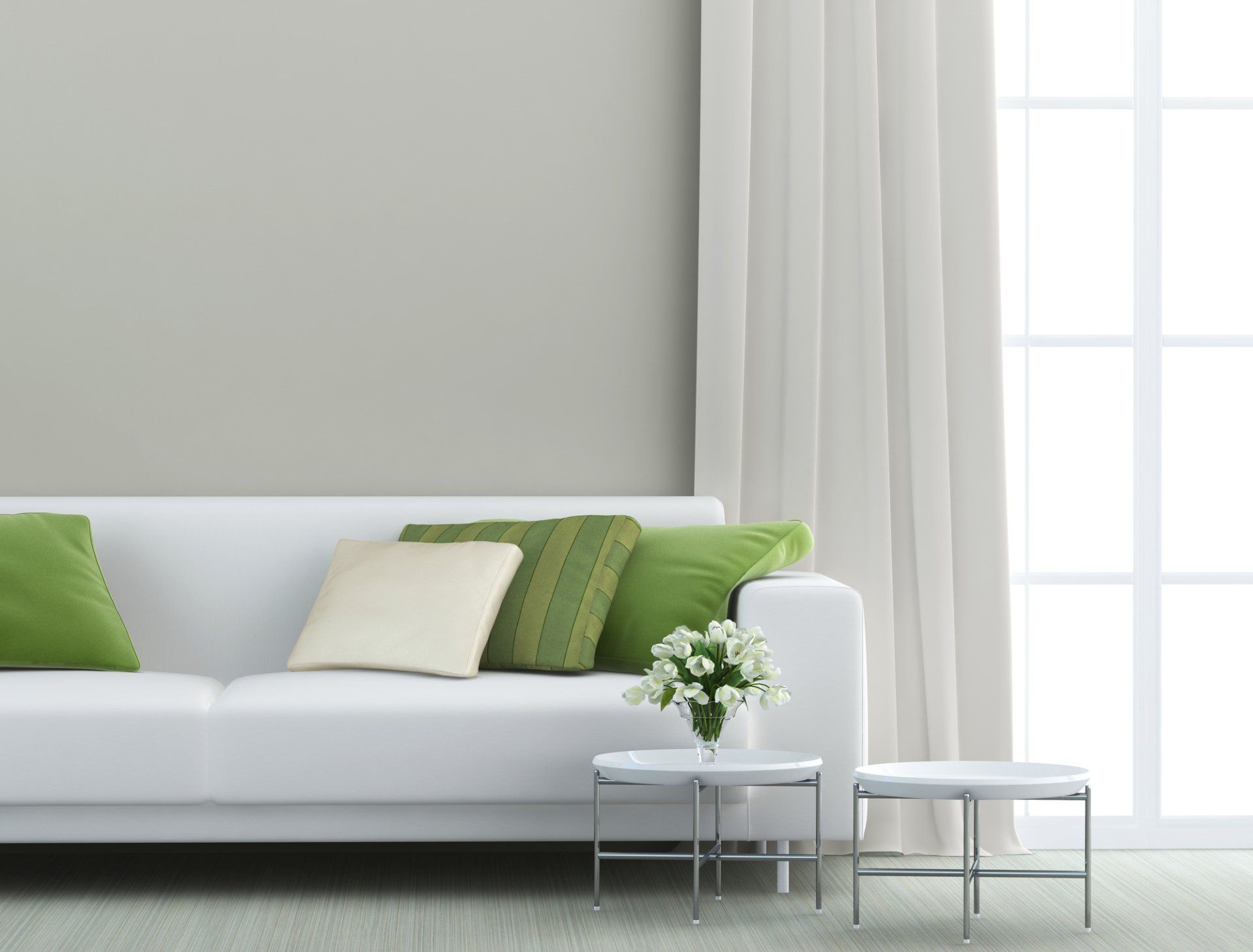 Formal lounge with white couch and green cushions, in front of white and chrome mini coffee tables with flowers, framed by formal white curtains opened over light filled window.